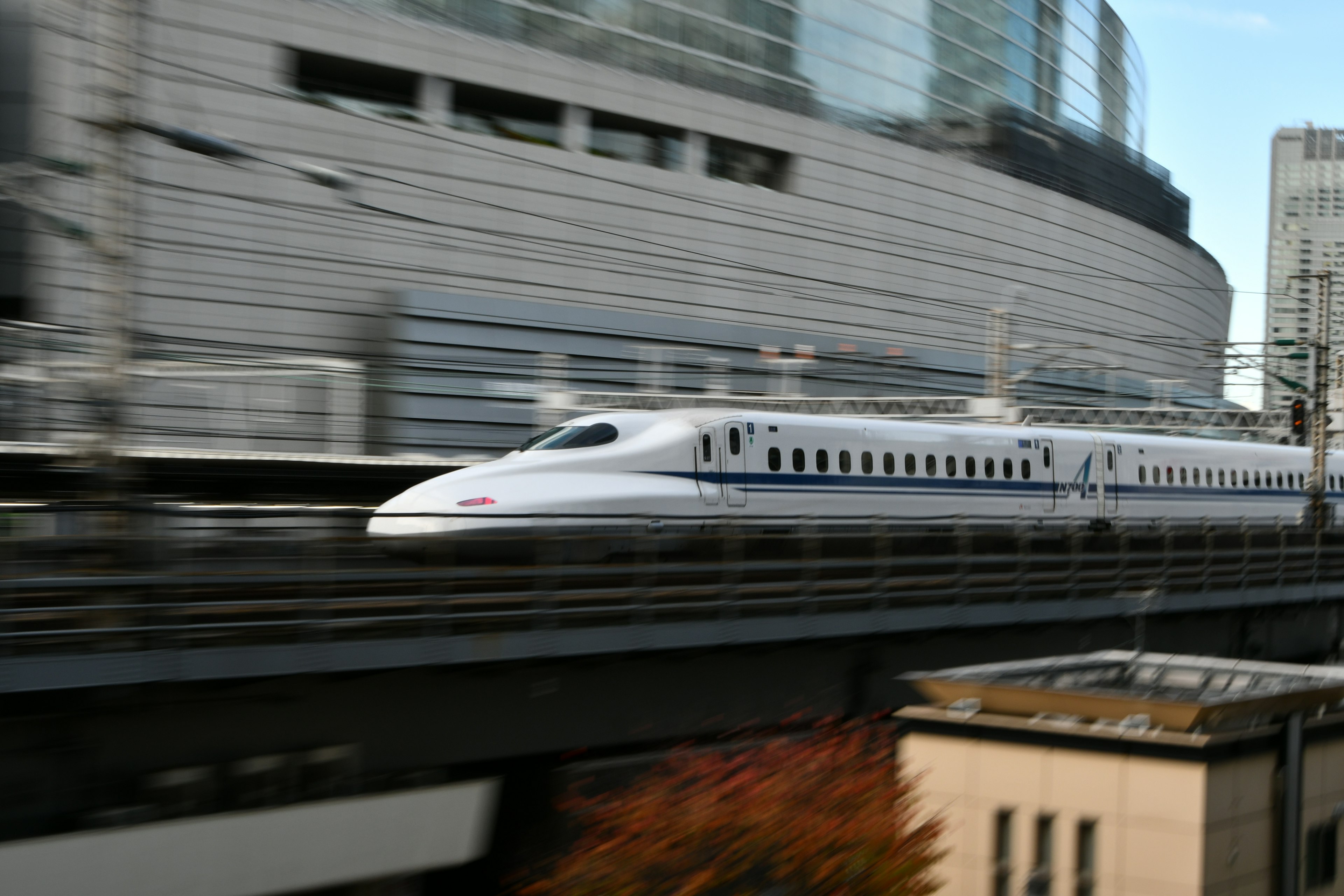 Shinkansen pasando rápidamente junto a edificios modernos en un entorno urbano