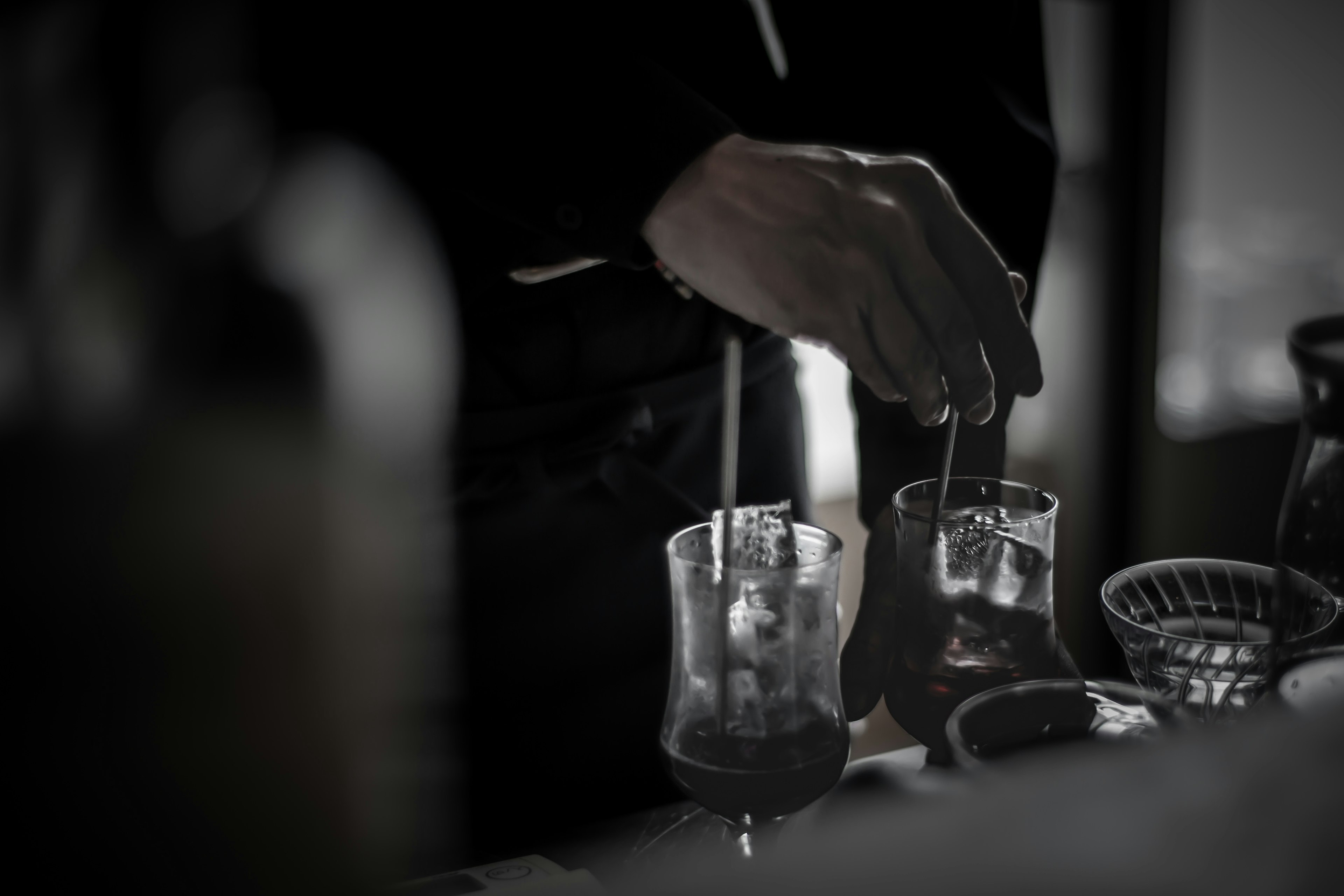 Close-up of a hand mixing cocktails at a bar with a dramatic black and white tone