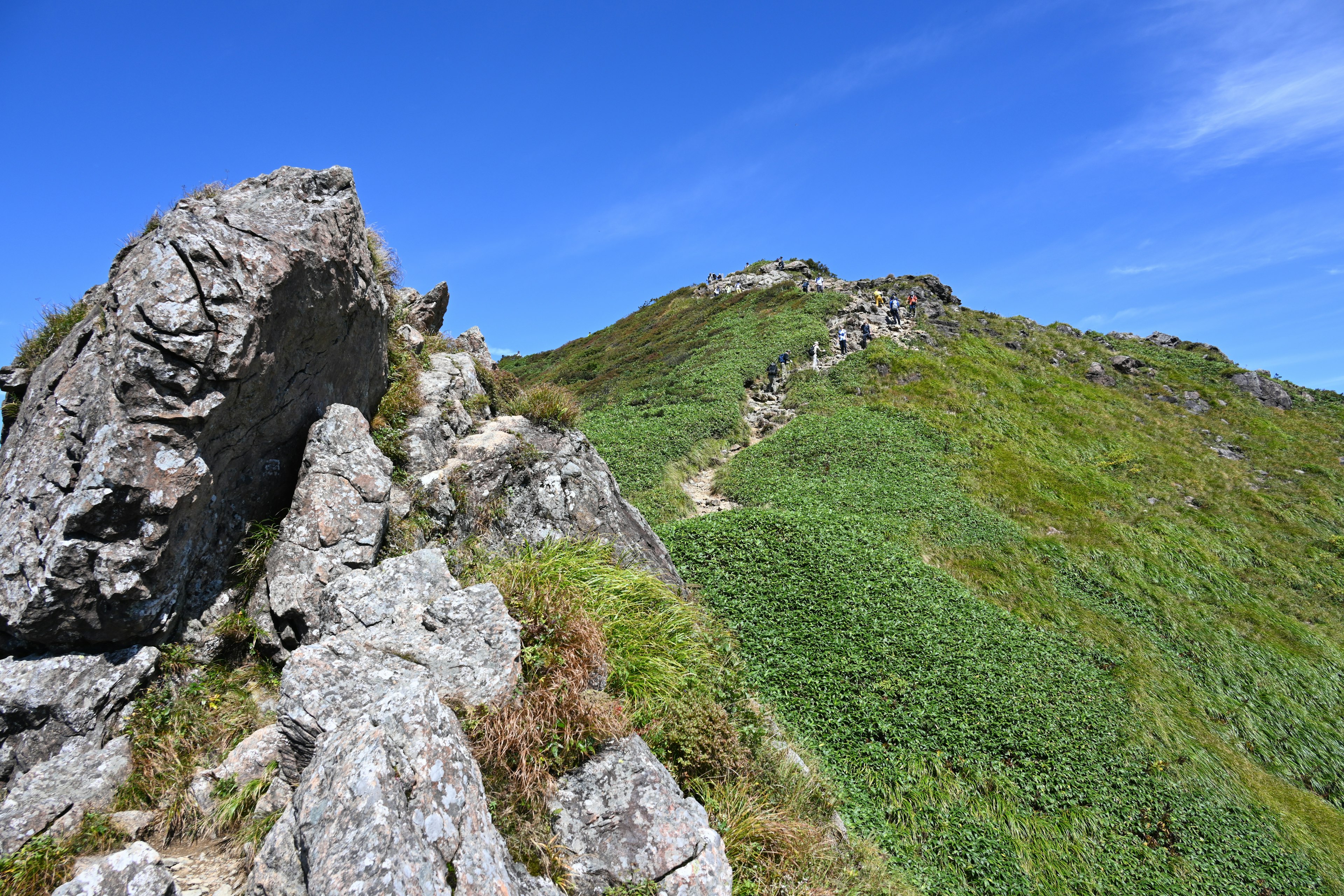 Mountain landscape with green grass and rocks under a blue sky and bright sunlight