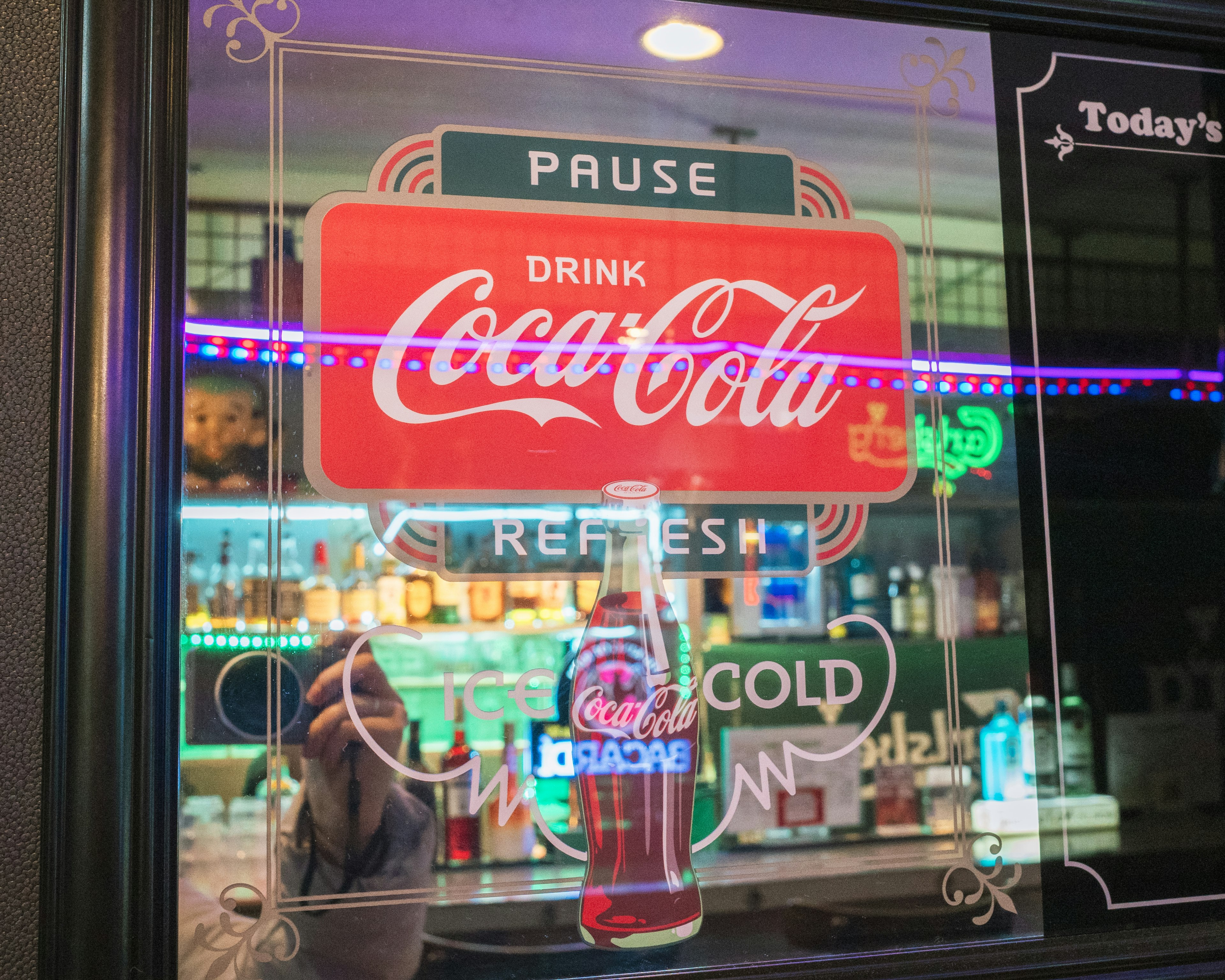 A retro Coca-Cola advertisement displayed on a window with a person standing in front