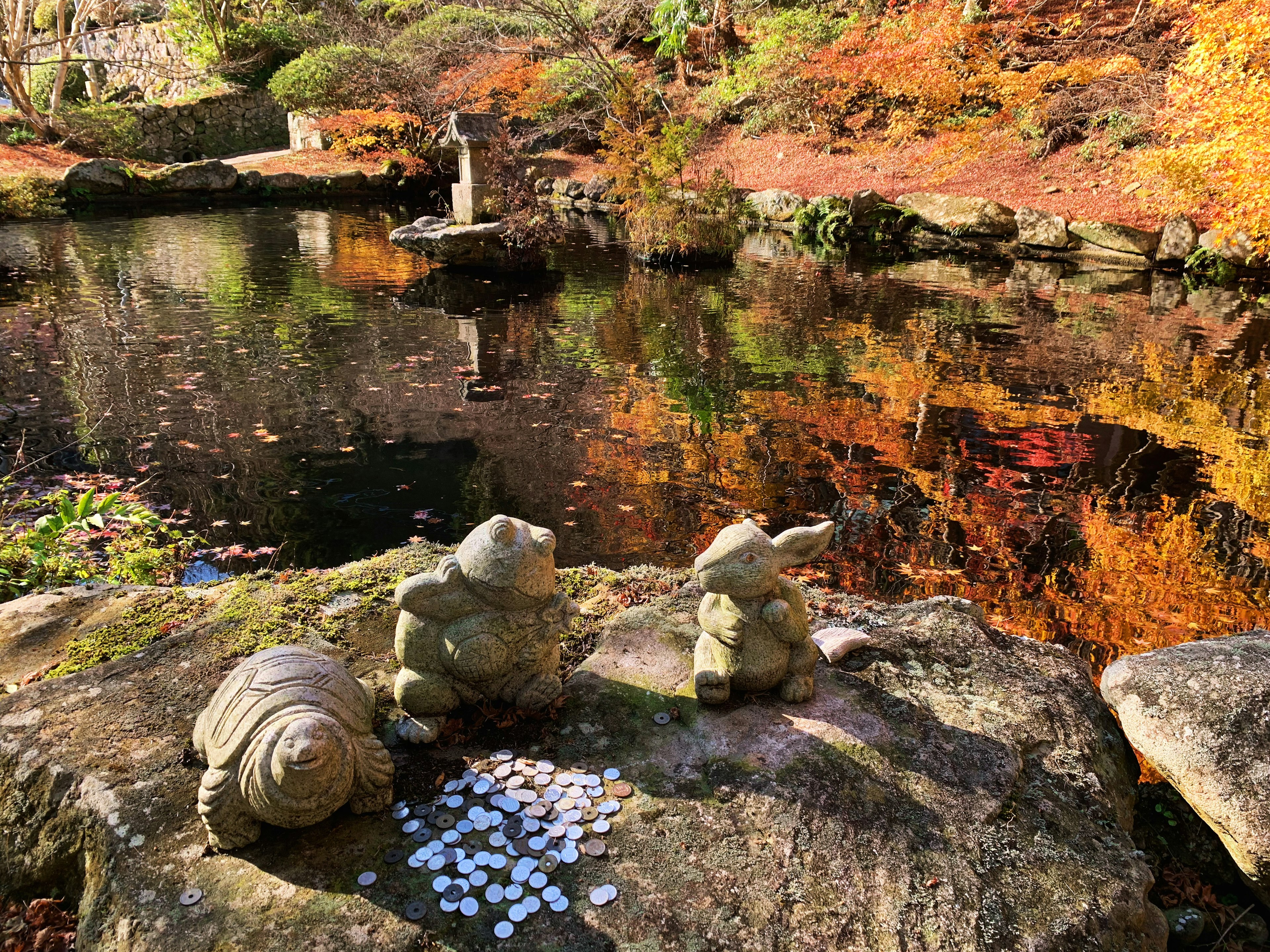 池のほとりに置かれた3つの石像と周囲の美しい秋の紅葉