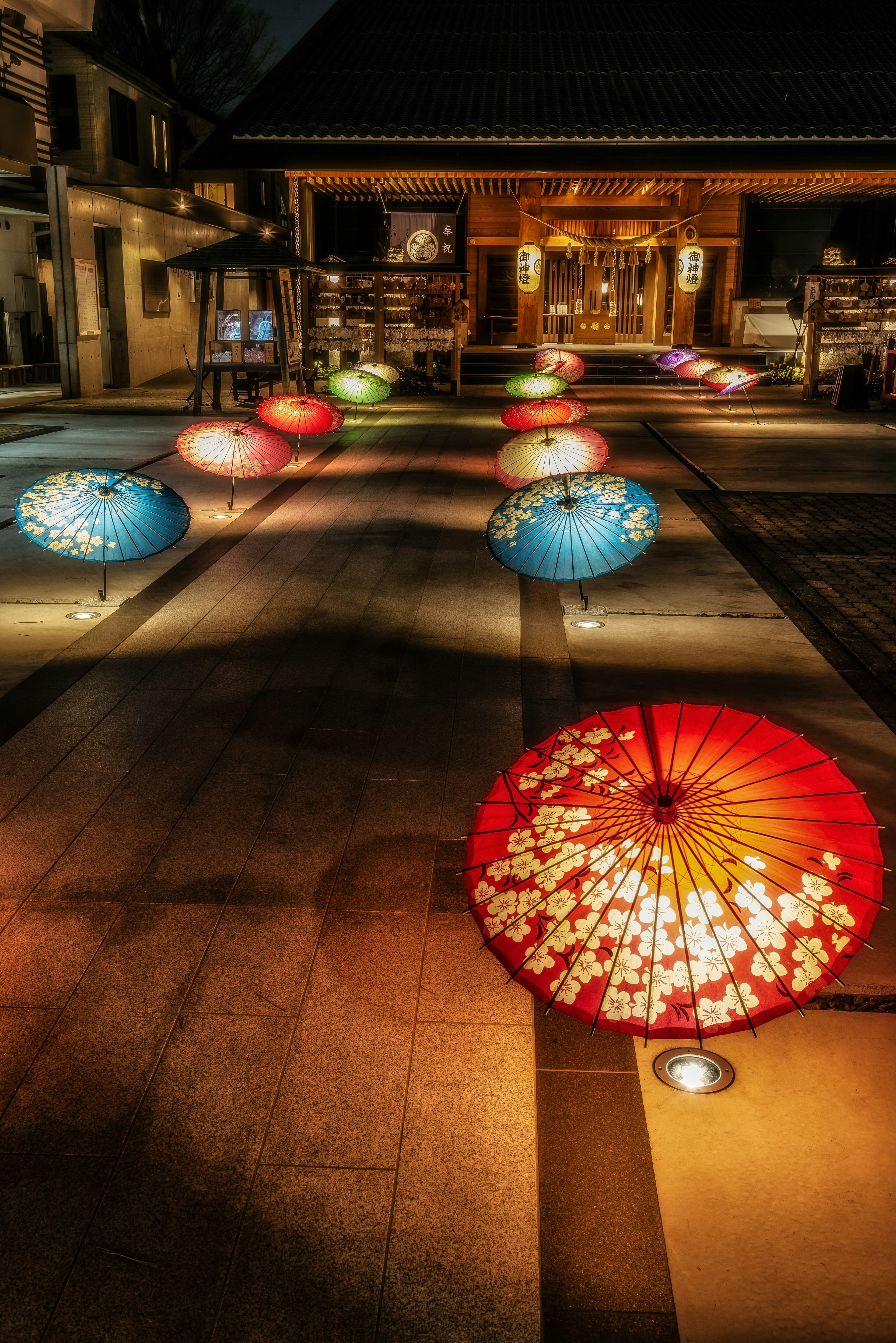 Sombrillas coloridas dispuestas frente a un templo por la noche con iluminación suave