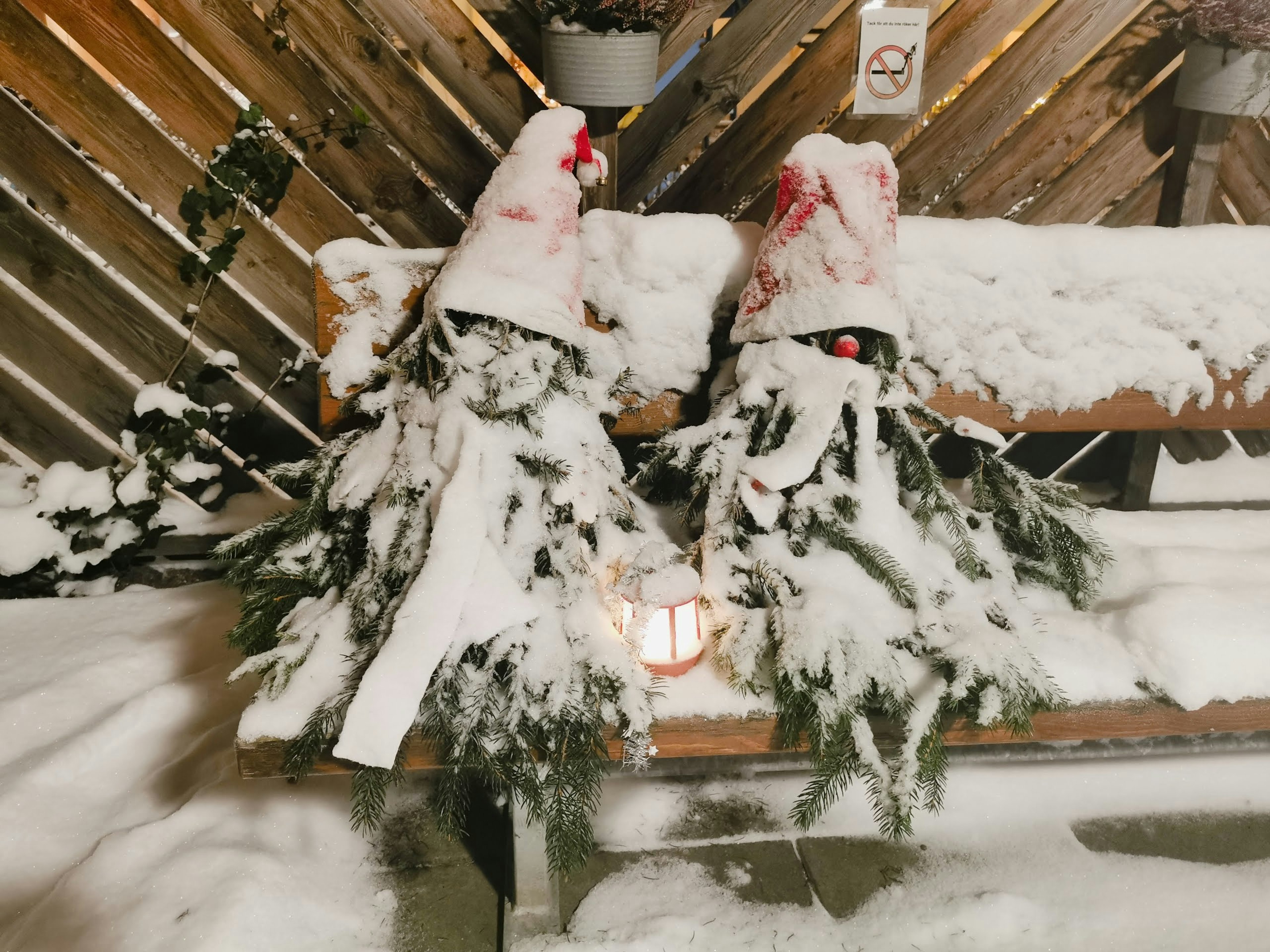 Two decorative figures made of snow-covered branches sitting on a bench