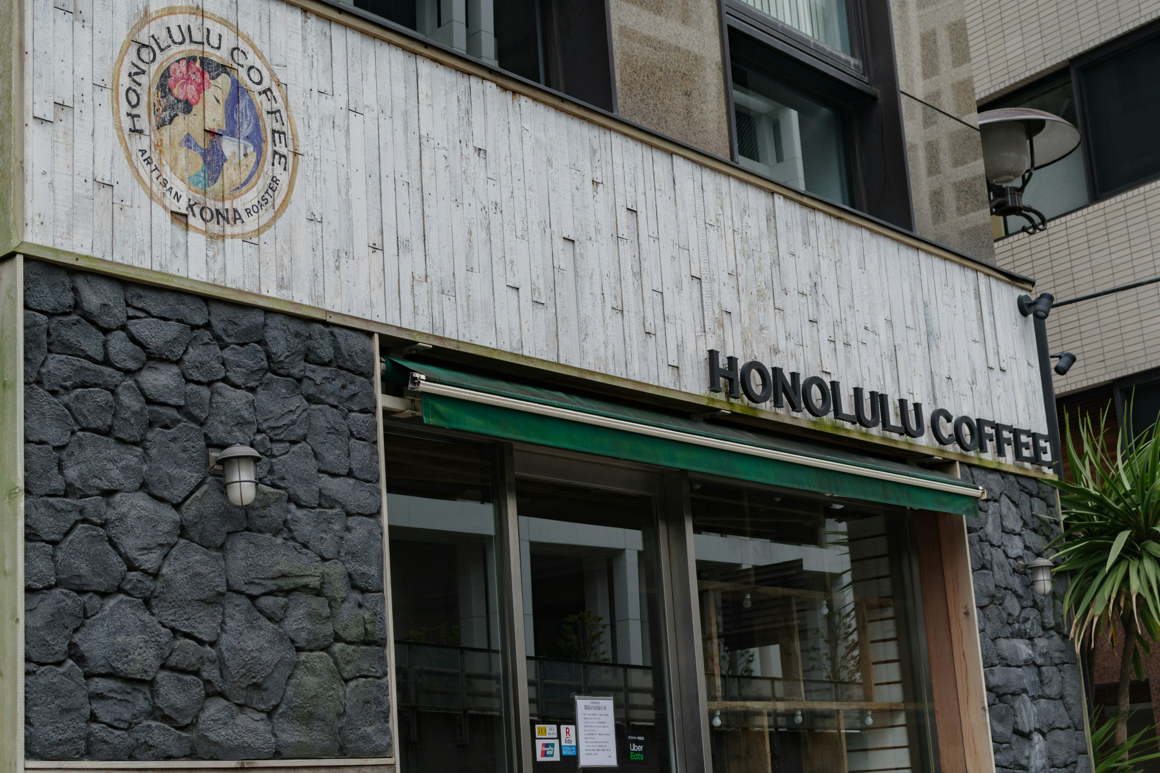 Exterior de la cafetería Honolulu con letrero de madera y pared de piedra