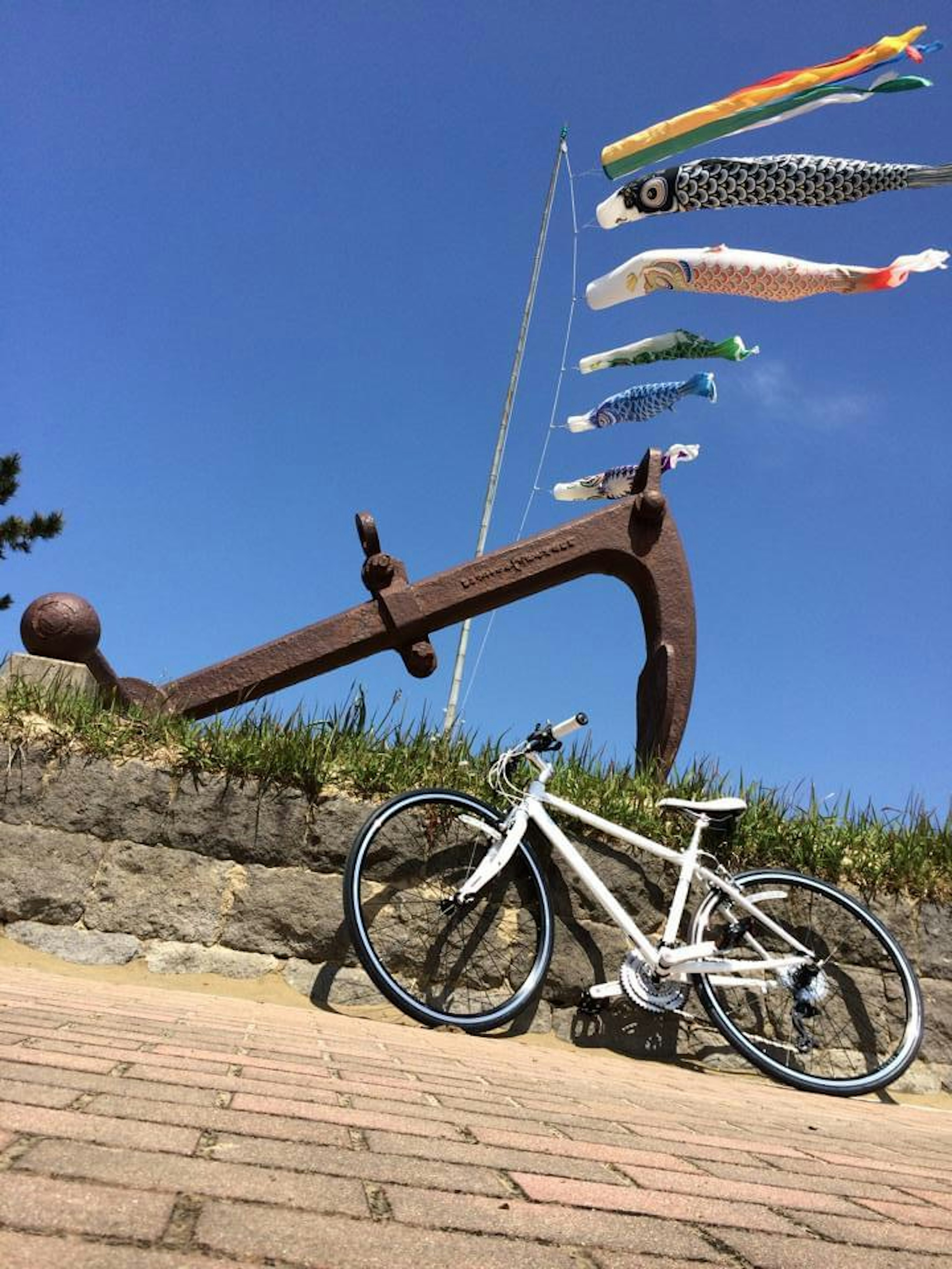 白い自転車と大きな鉄のアンカーが青い空の下にある風景