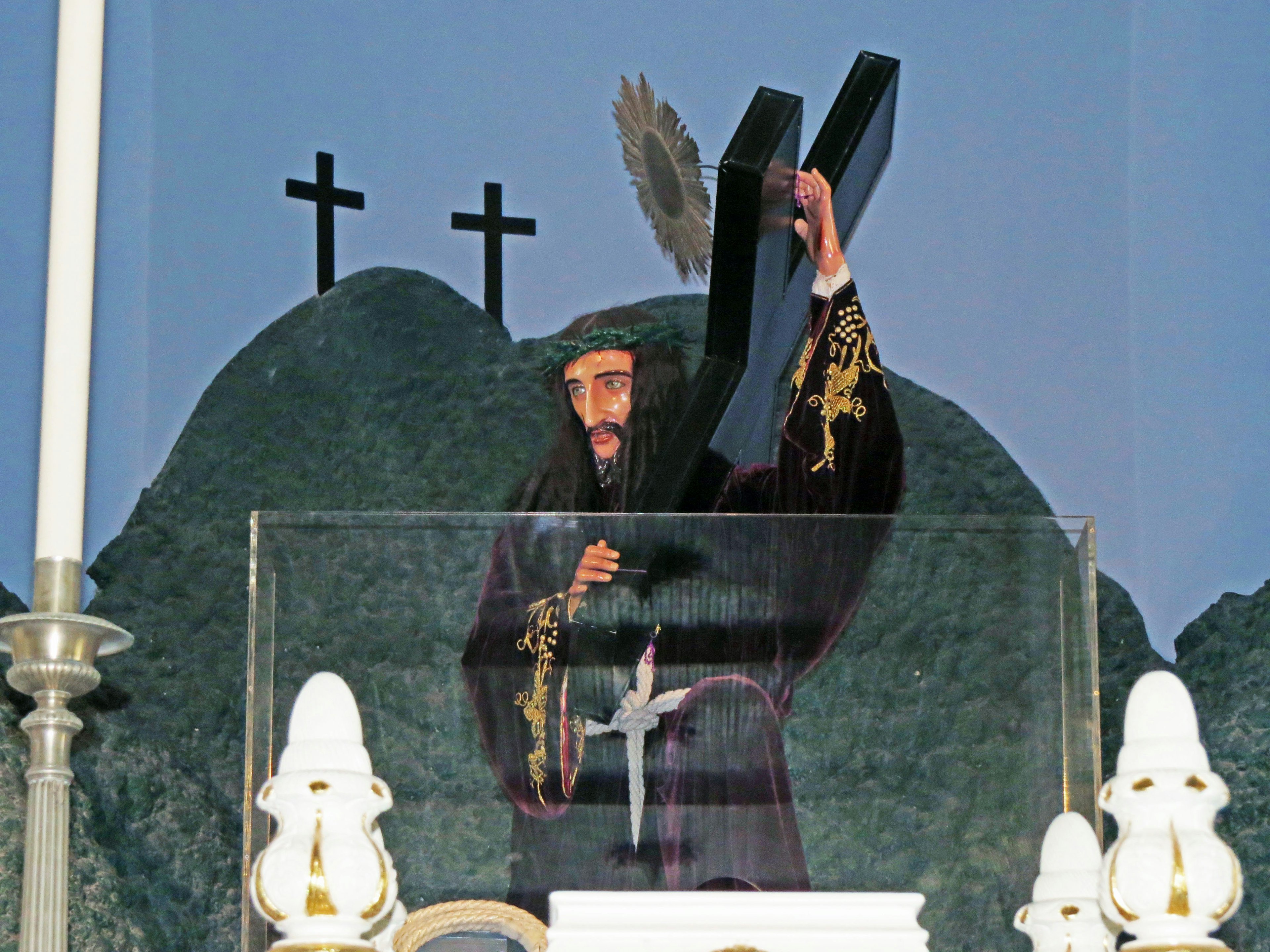 A clergyman holding a cross in front of an altar with a mountainous backdrop