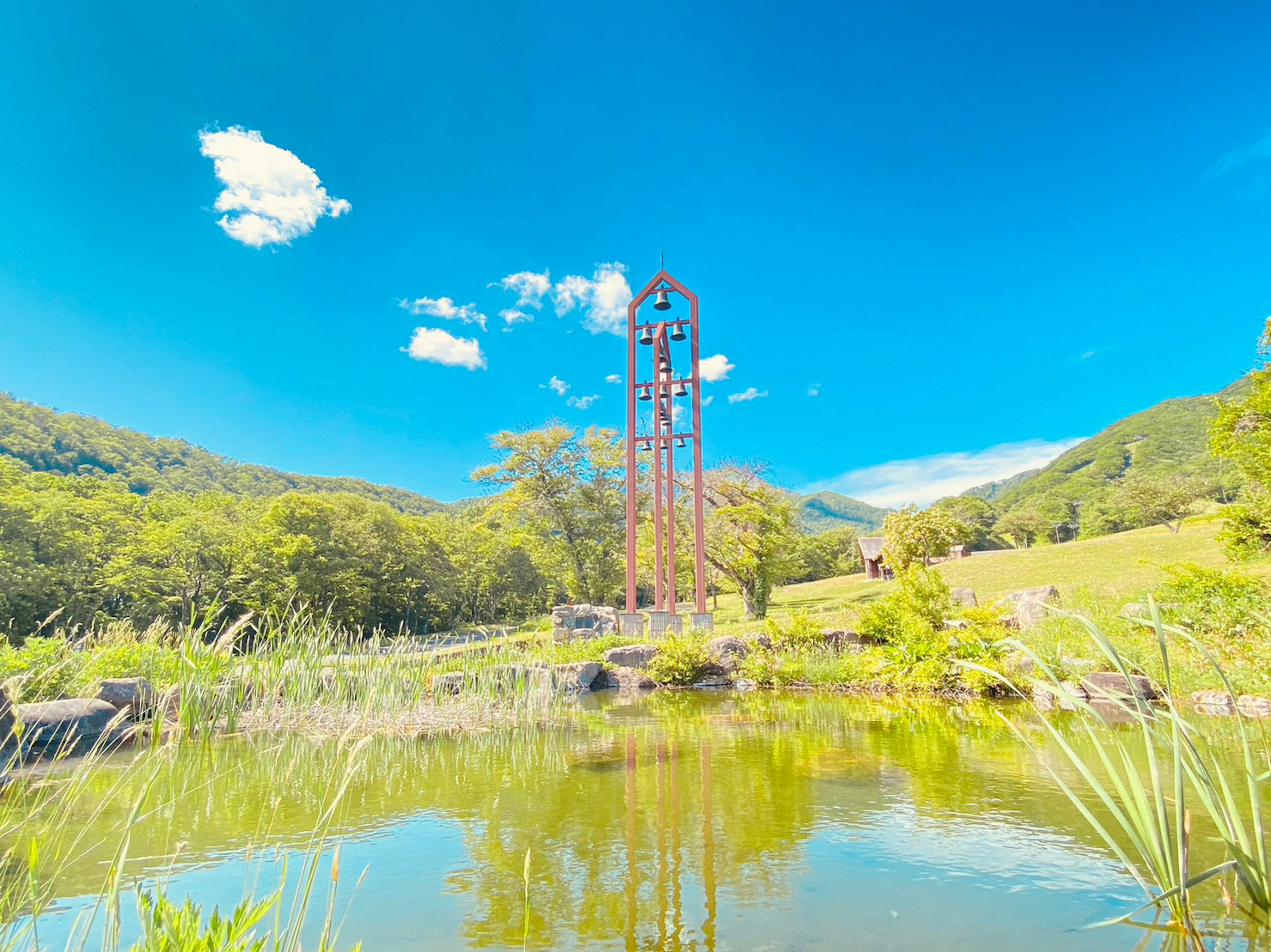 Landscape featuring a pond and tall metal towers against a backdrop of blue sky and green mountains