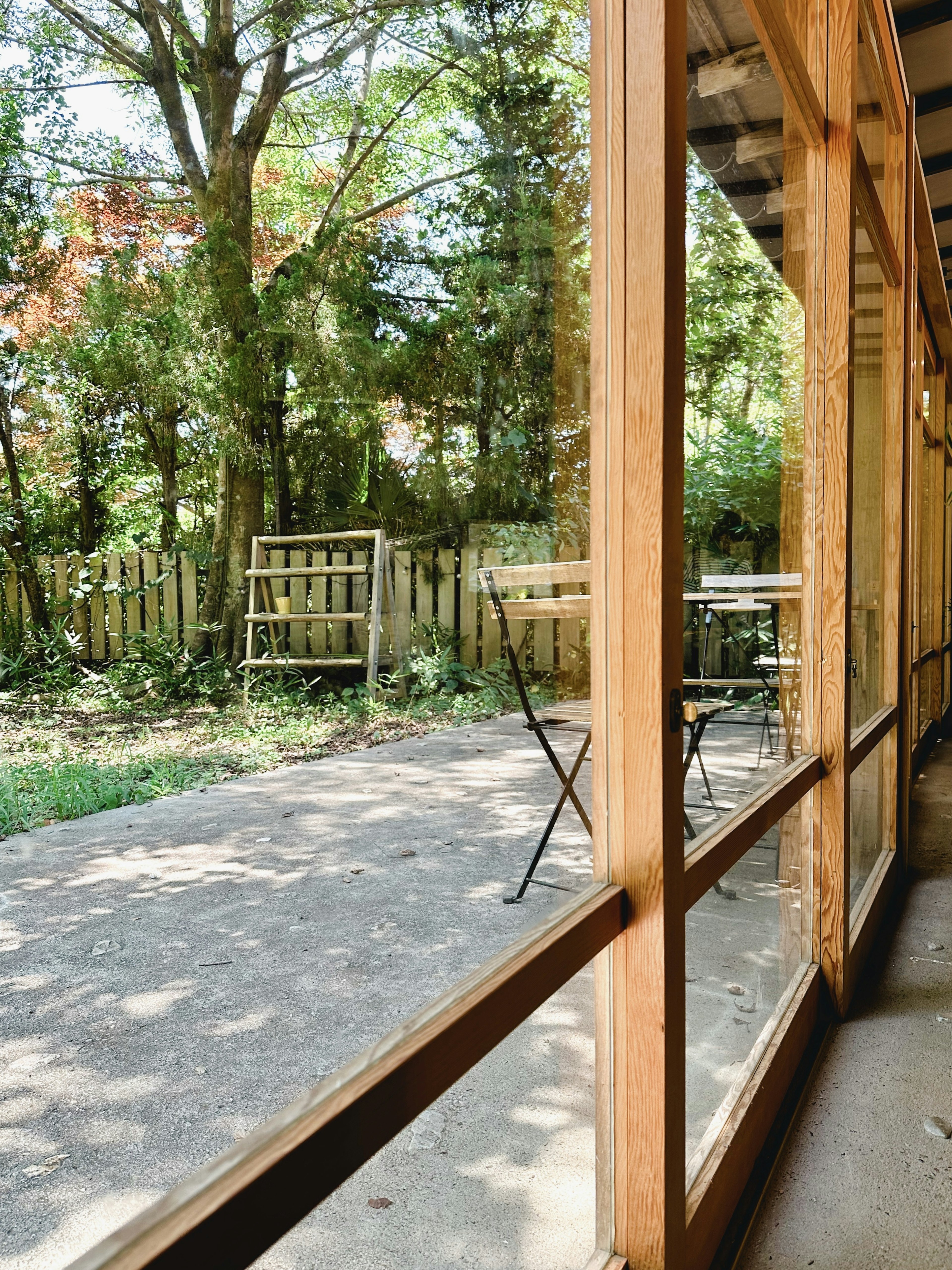 Marco de ventana de madera mostrando un jardín exuberante con una pequeña mesa y sillas