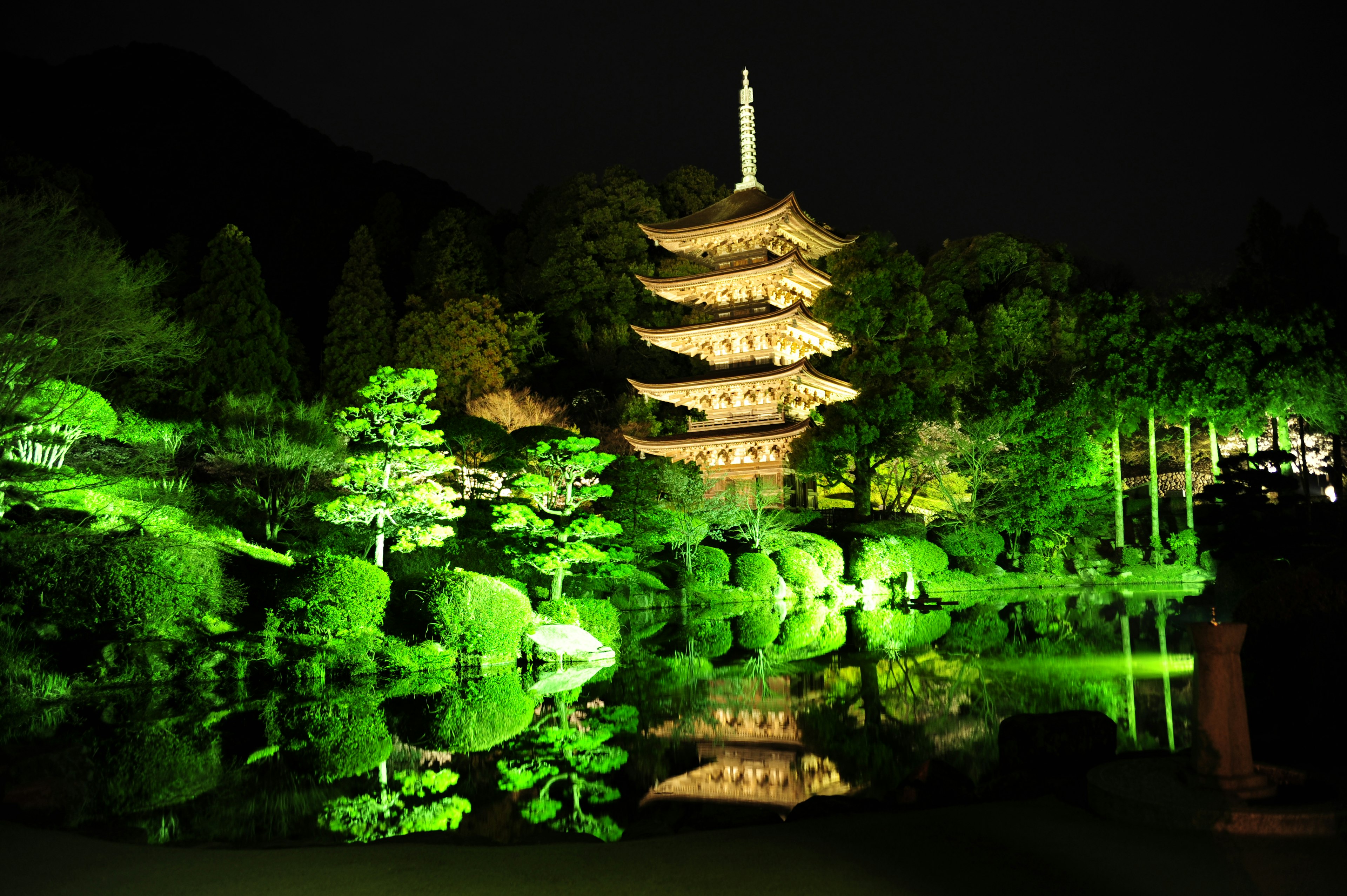 Illuminated pagoda at night with green lights and reflections in the pond