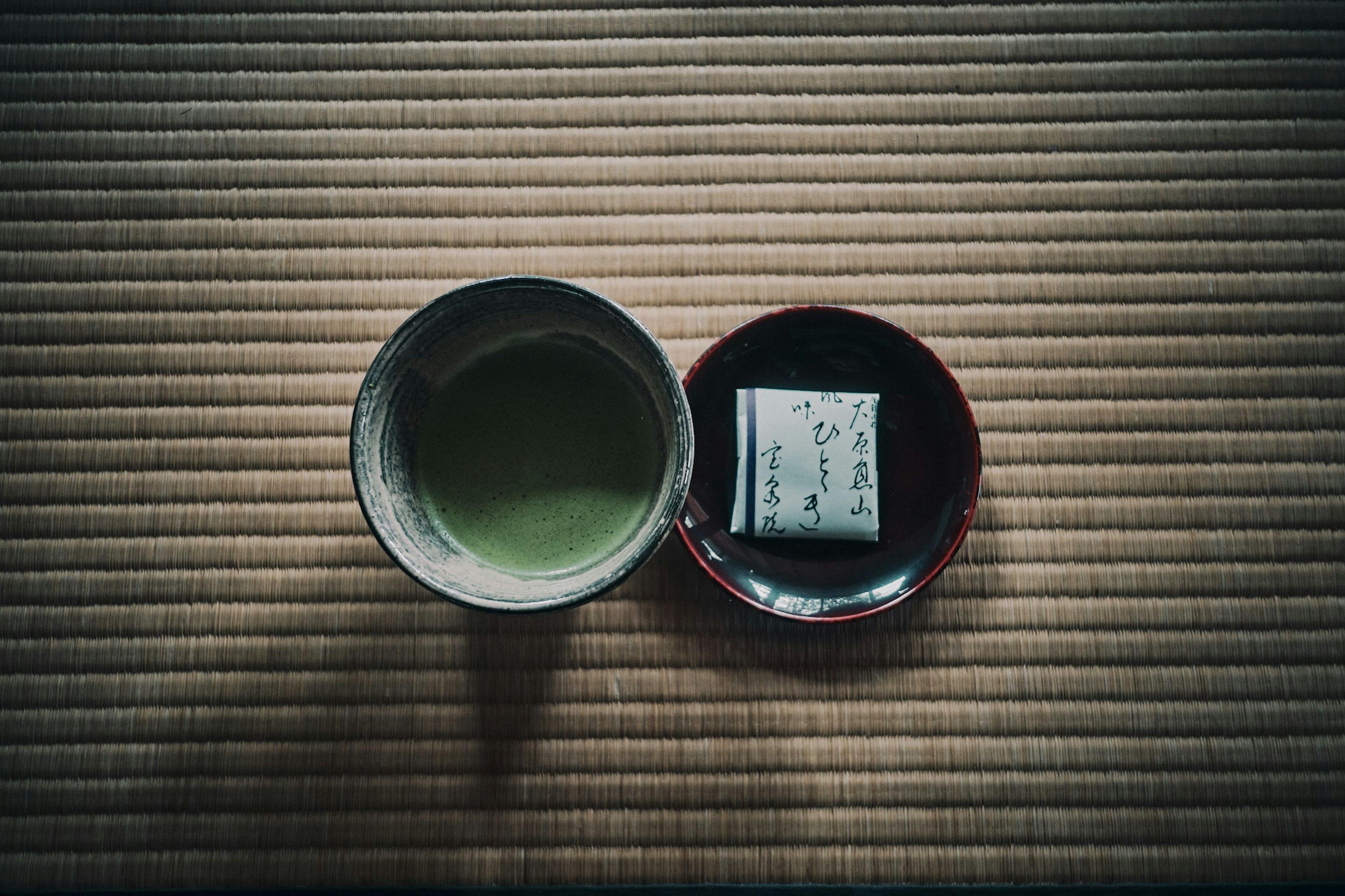 Una presentación de té japonés tradicional con té verde y un dulce sobre un tatami