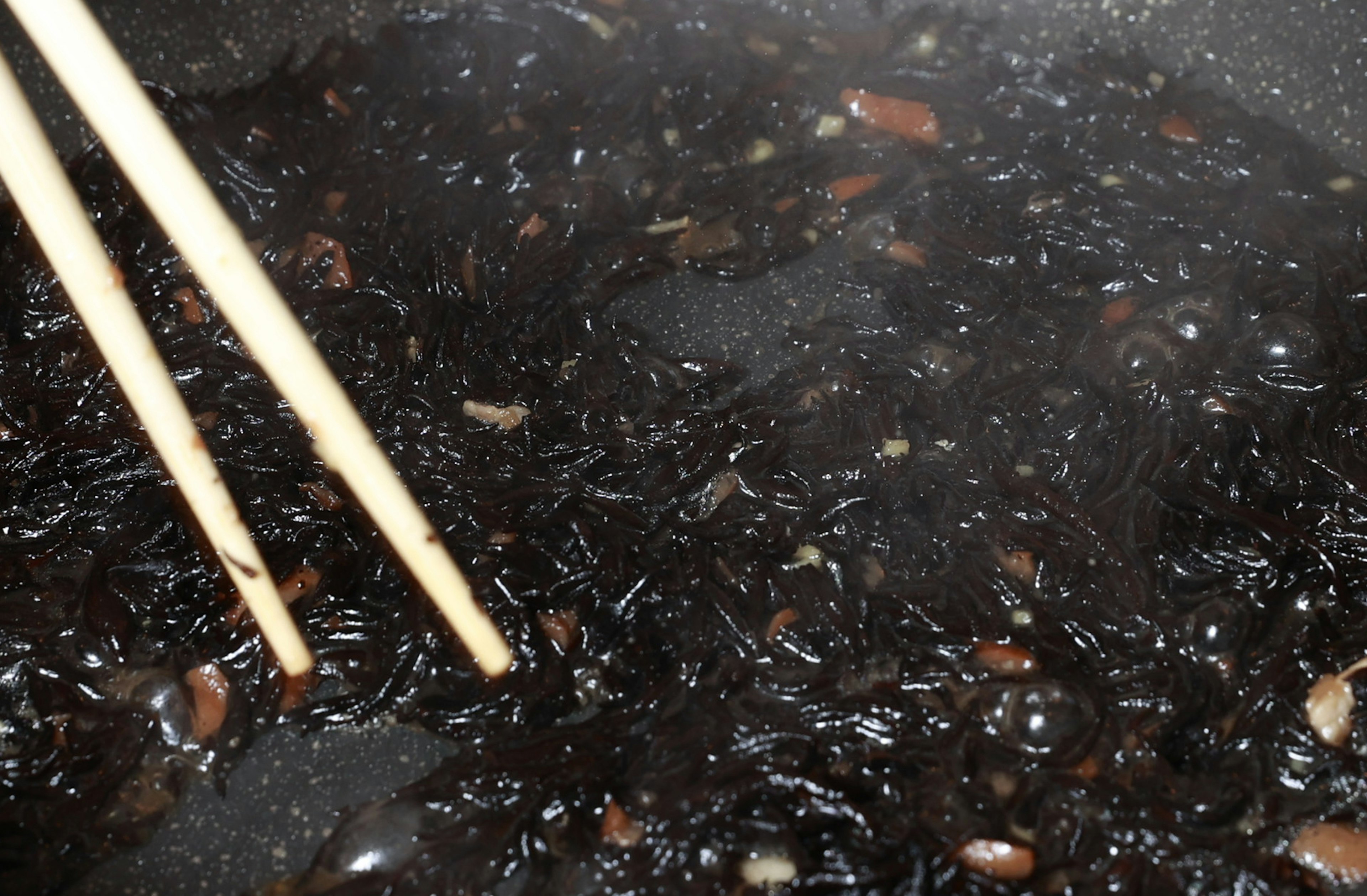 Close-up rumput laut hitam dalam panci dengan sumpit kayu