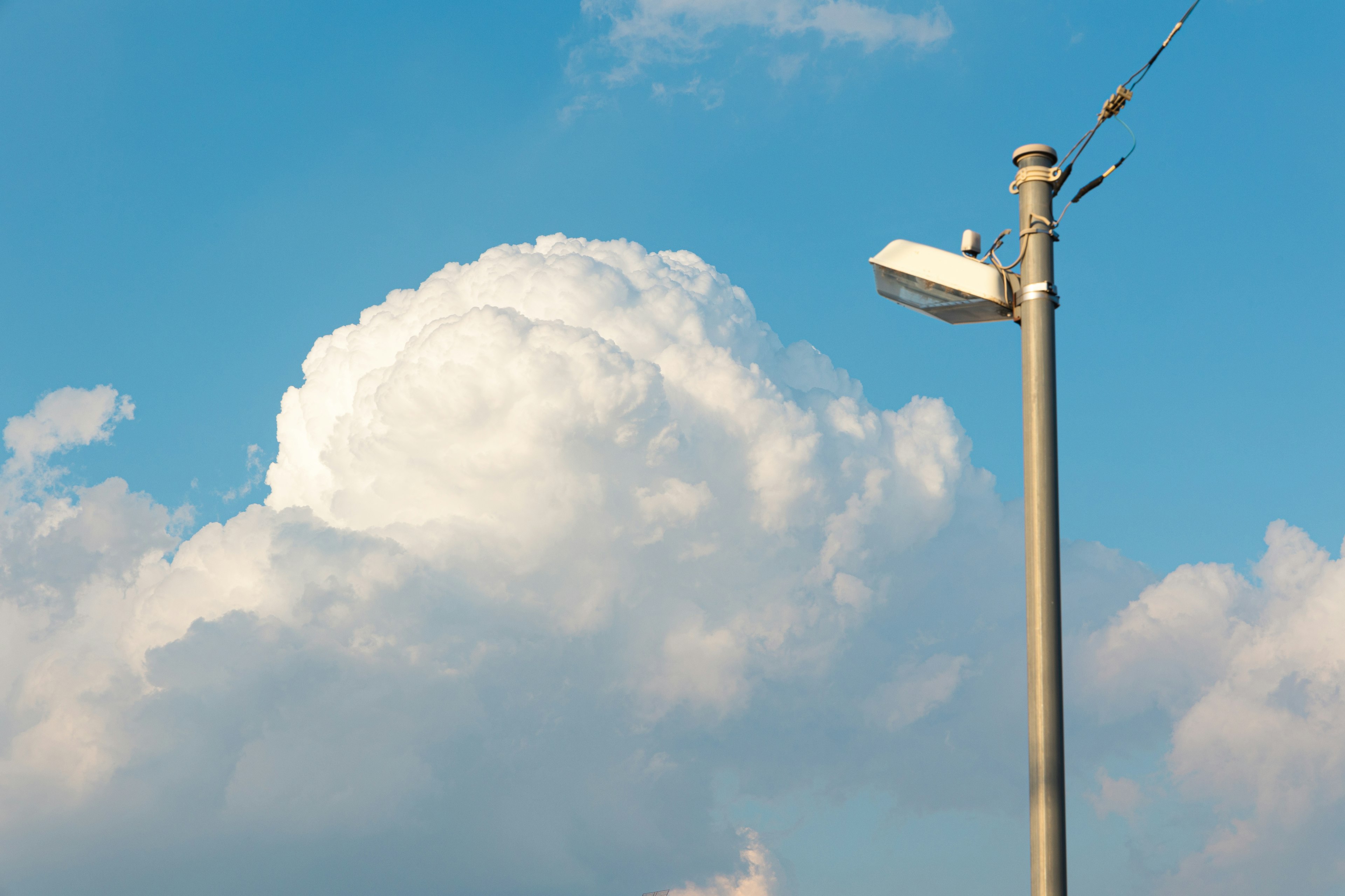 Una nube blanca bajo un cielo azul con una farola