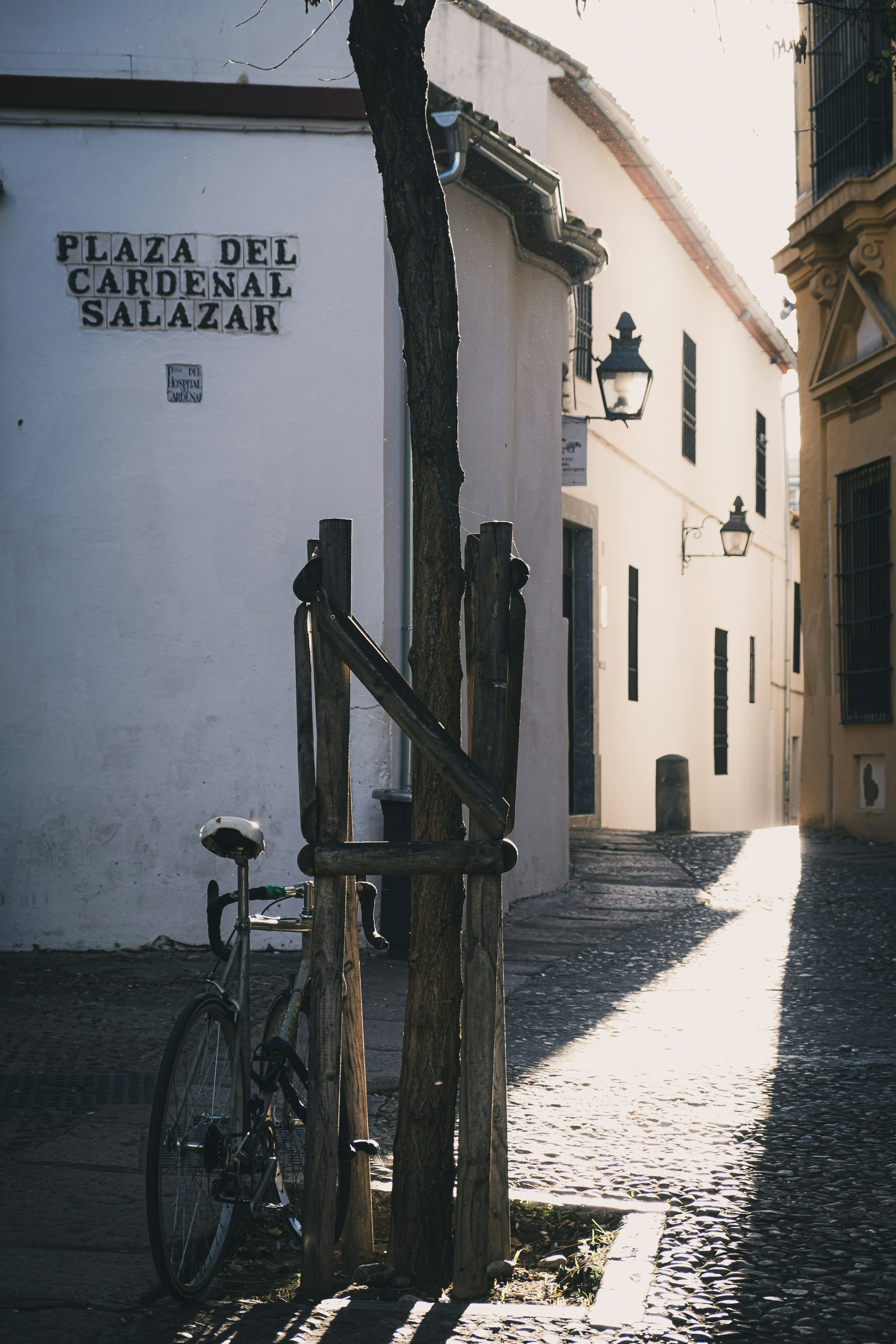 Vélo garé près d'un poteau en bois dans une ruelle calme avec le panneau Plaza del Cardenal Salazar