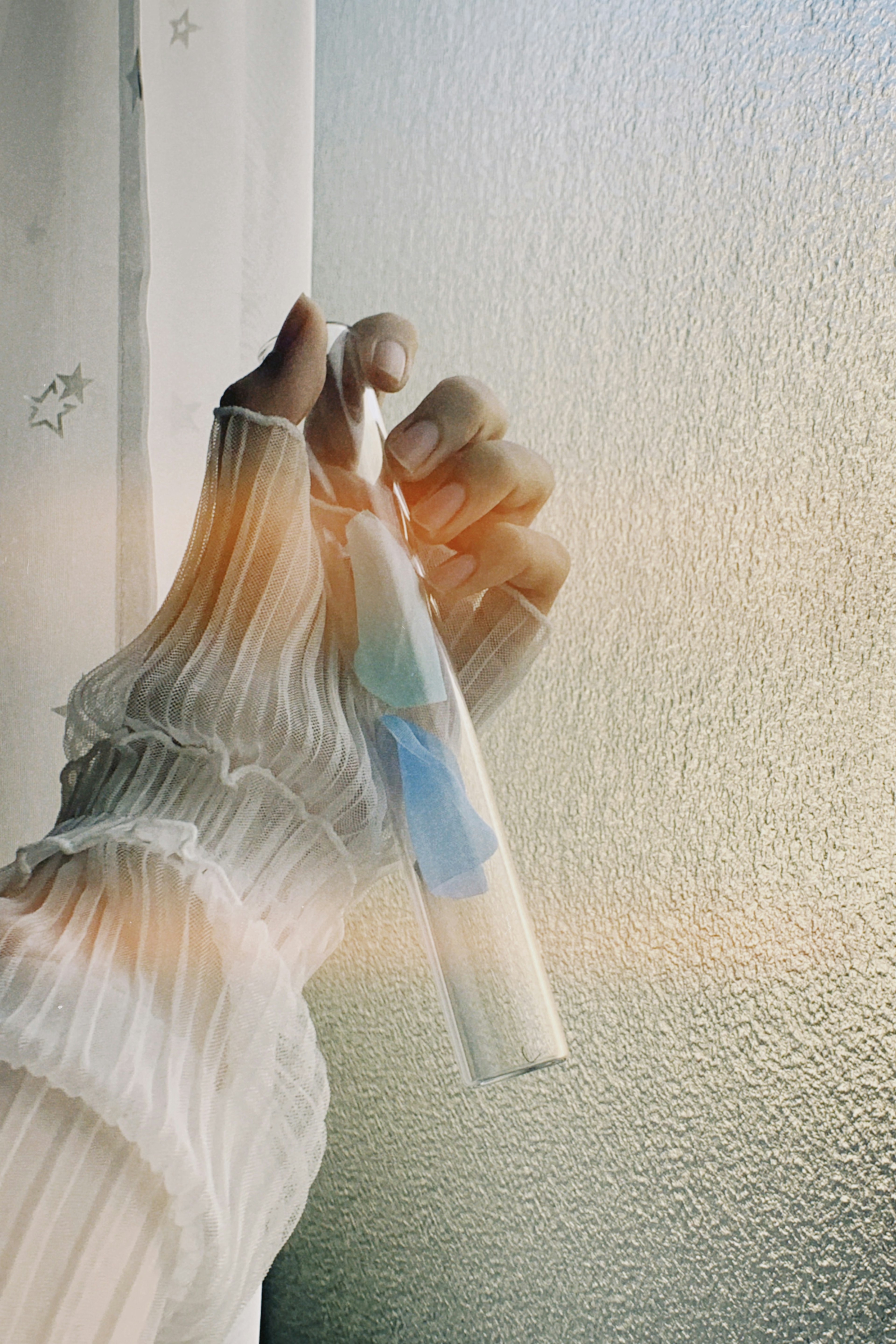 Una mano sosteniendo una botella clara cerca de una ventana en luz suave