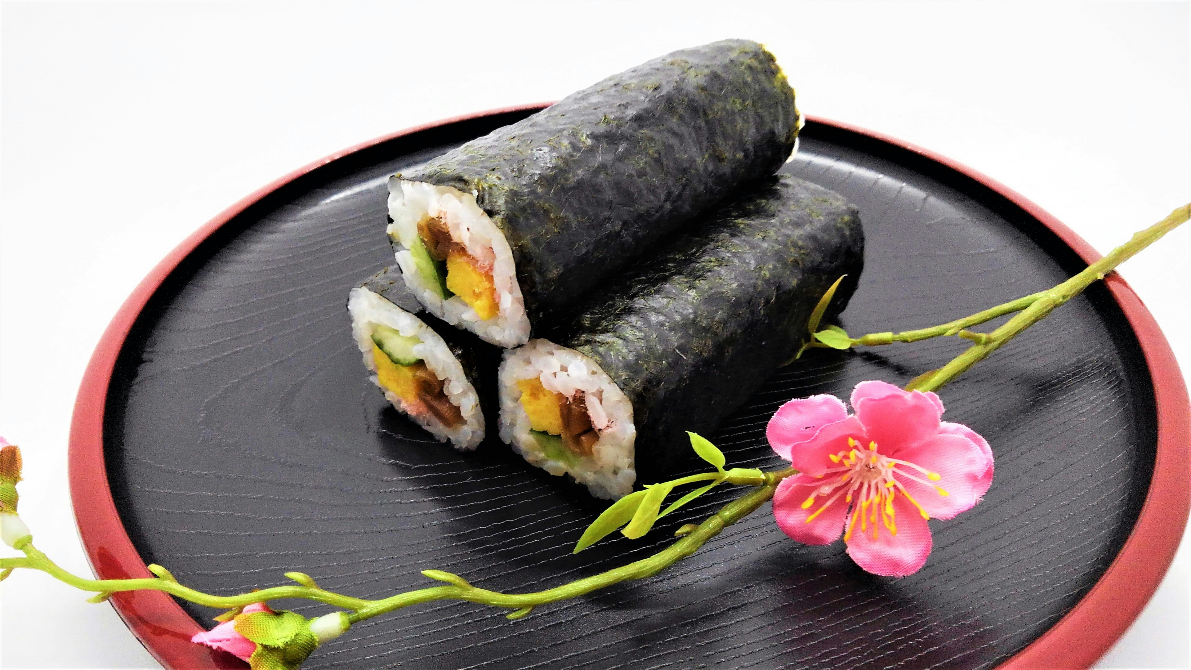 Sushi rolls displayed on a black plate with a decorative cherry blossom