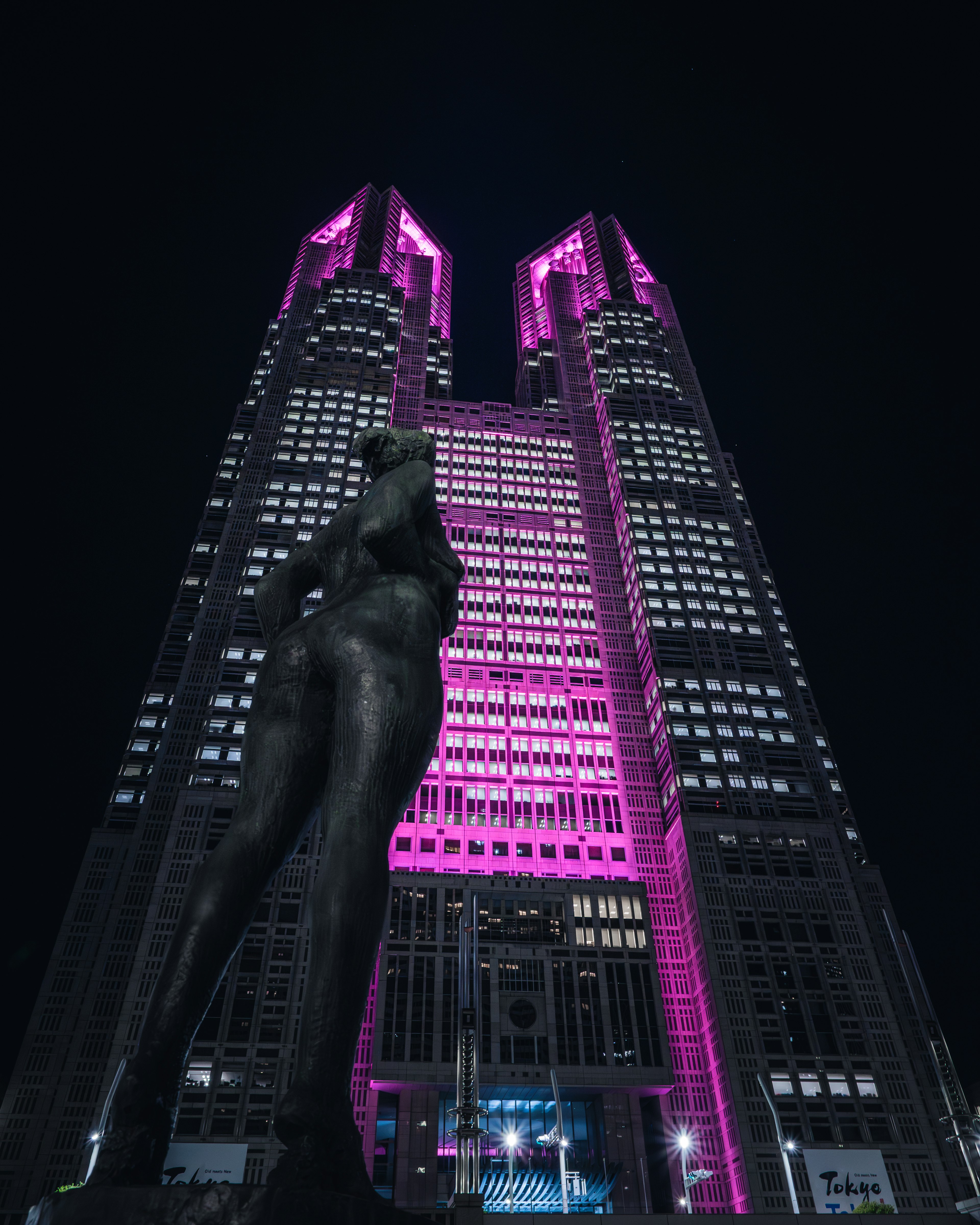 Tokyo Metropolitan Government building illuminated in pink at night with a statue in the foreground