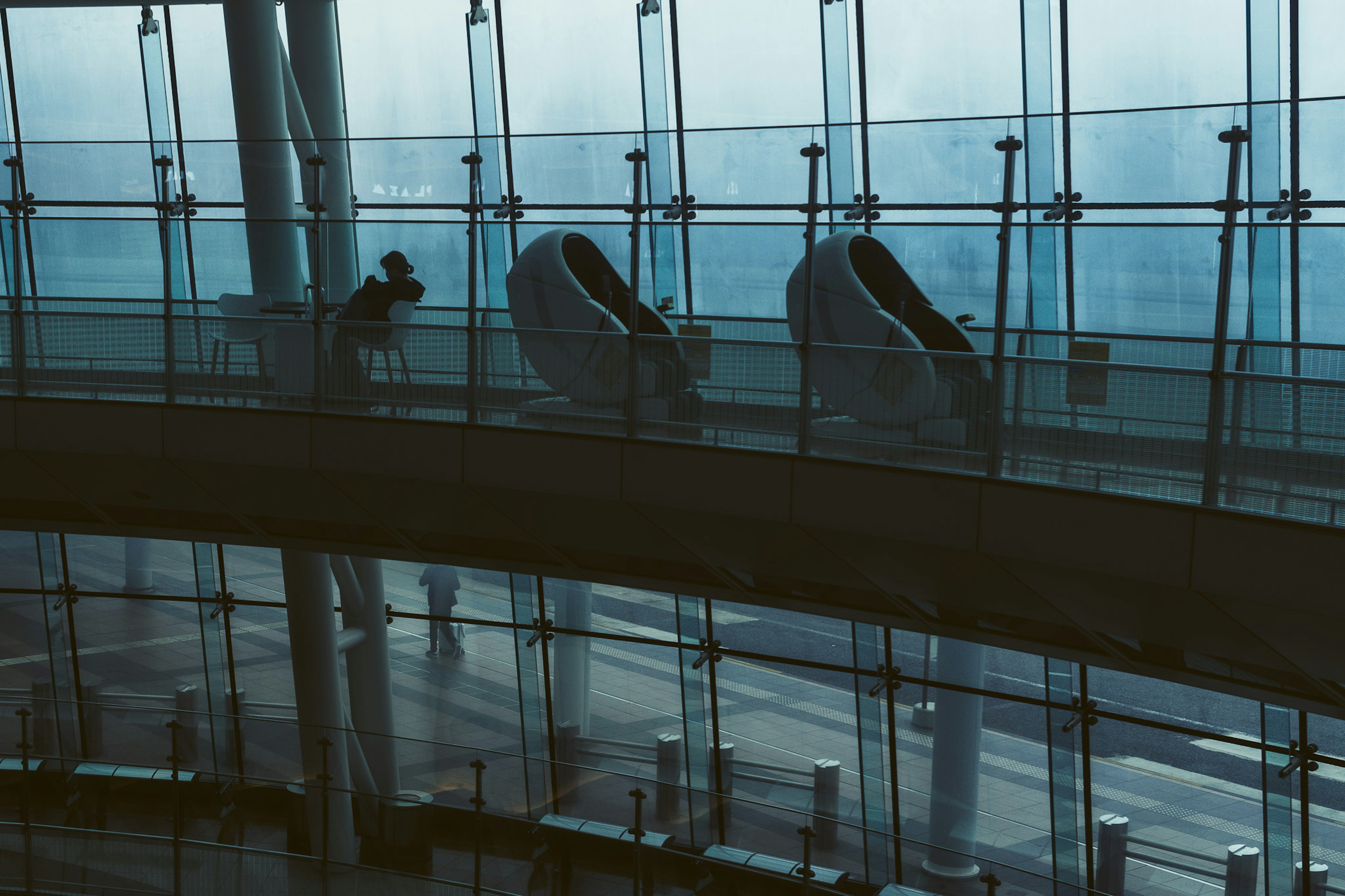 Silhouette di persone lungo un corridoio di vetro con posti a sedere in un aeroporto