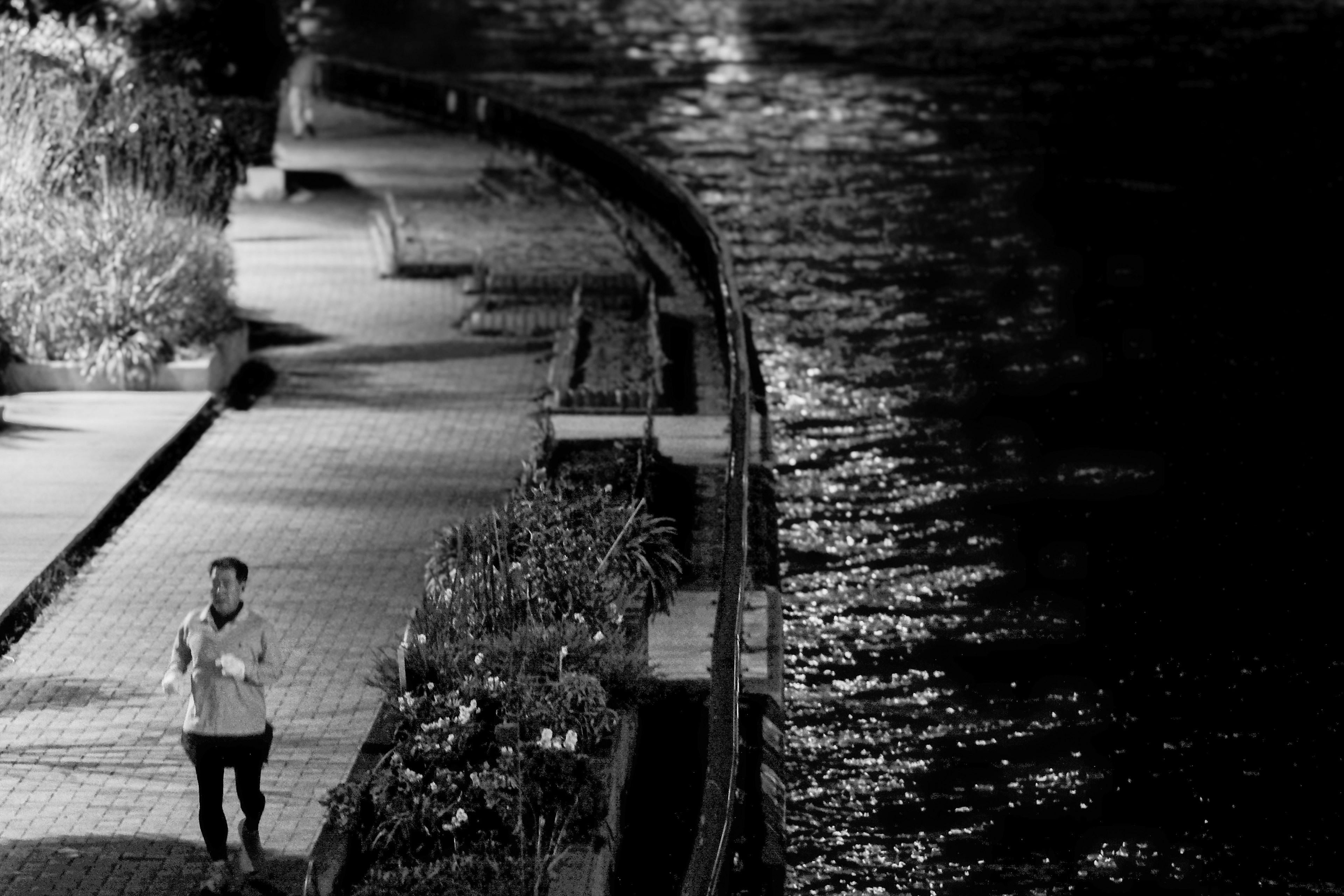 A man walking along a riverside promenade at night with streetlights reflecting on the water