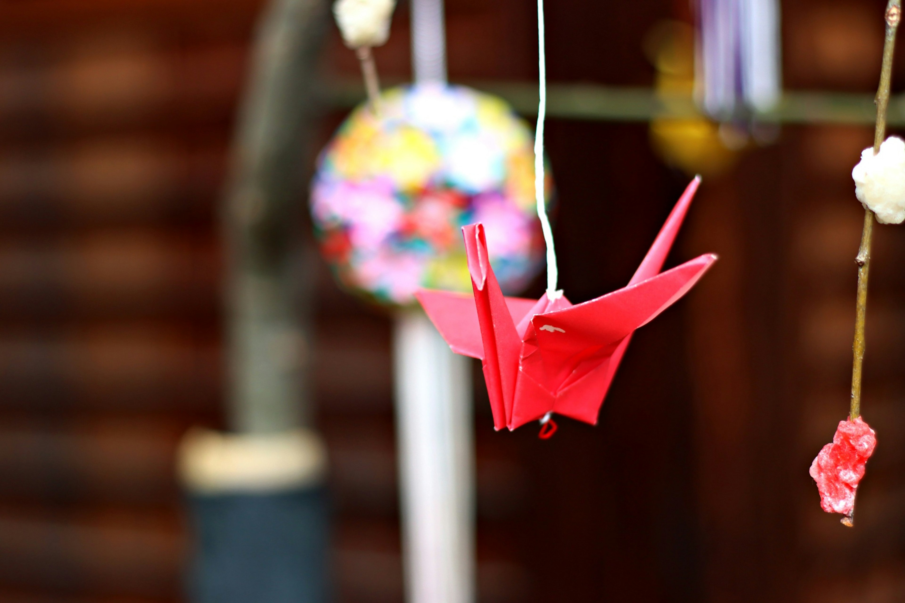 A red origami crane hanging with colorful decorations in the background