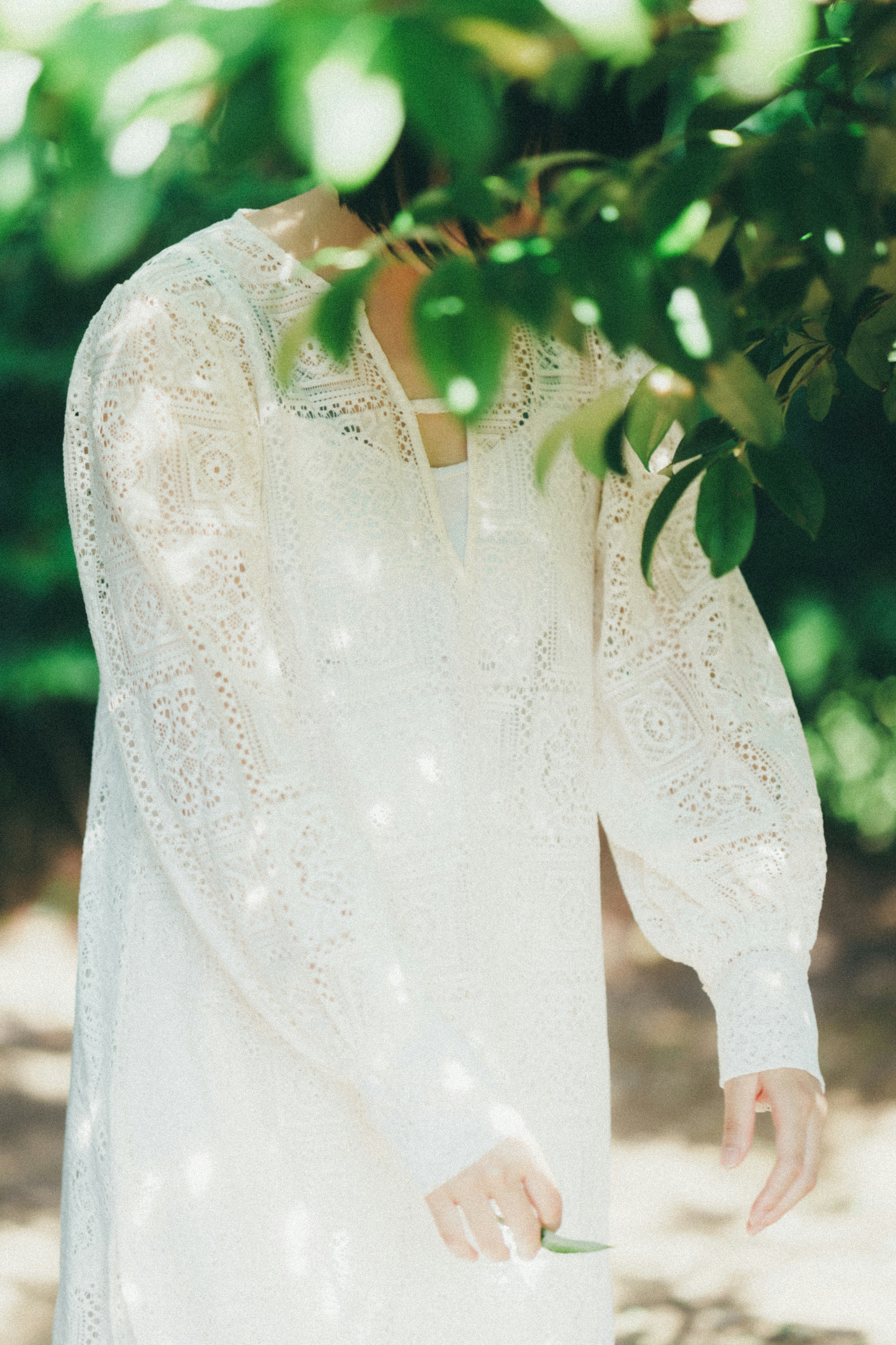 A person wearing a white dress stands among green leaves