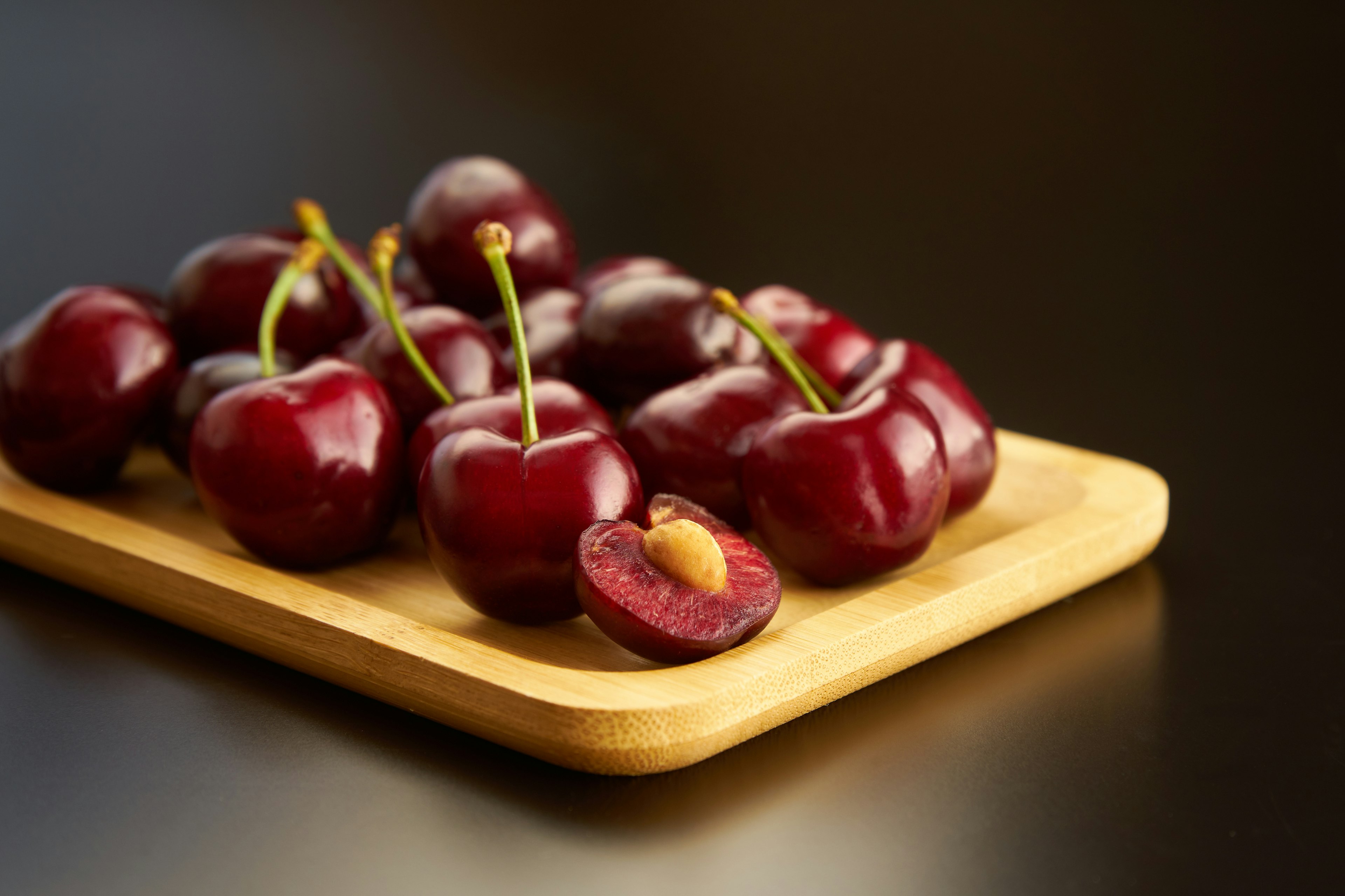 Fresh cherries arranged on a wooden tray with a sliced plum