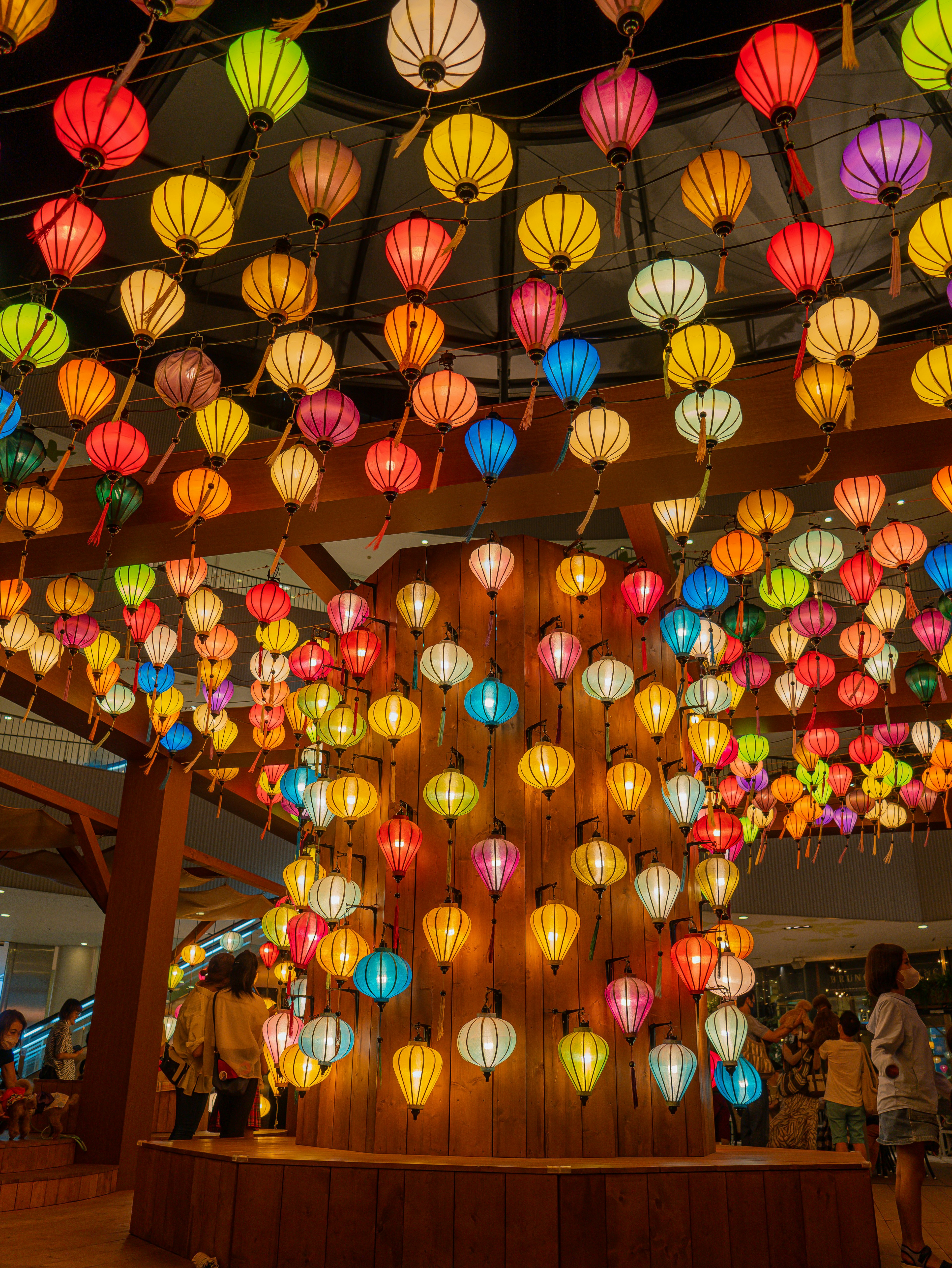 Ruang cerah yang dipenuhi lampion berwarna-warni menggantung dari langit-langit di sekitar tiang kayu