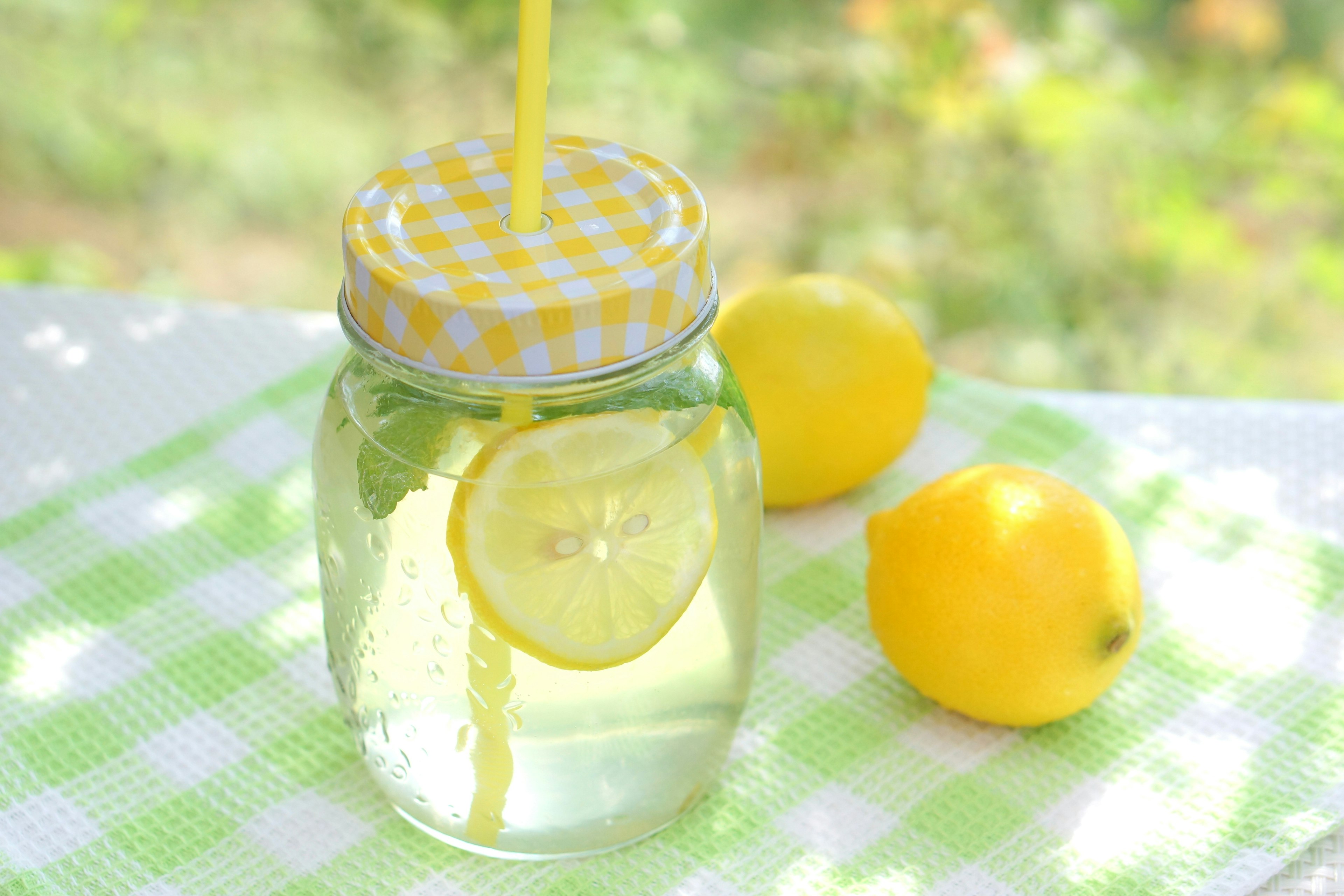 A clear drink jar with lemon and a straw alongside fresh lemons