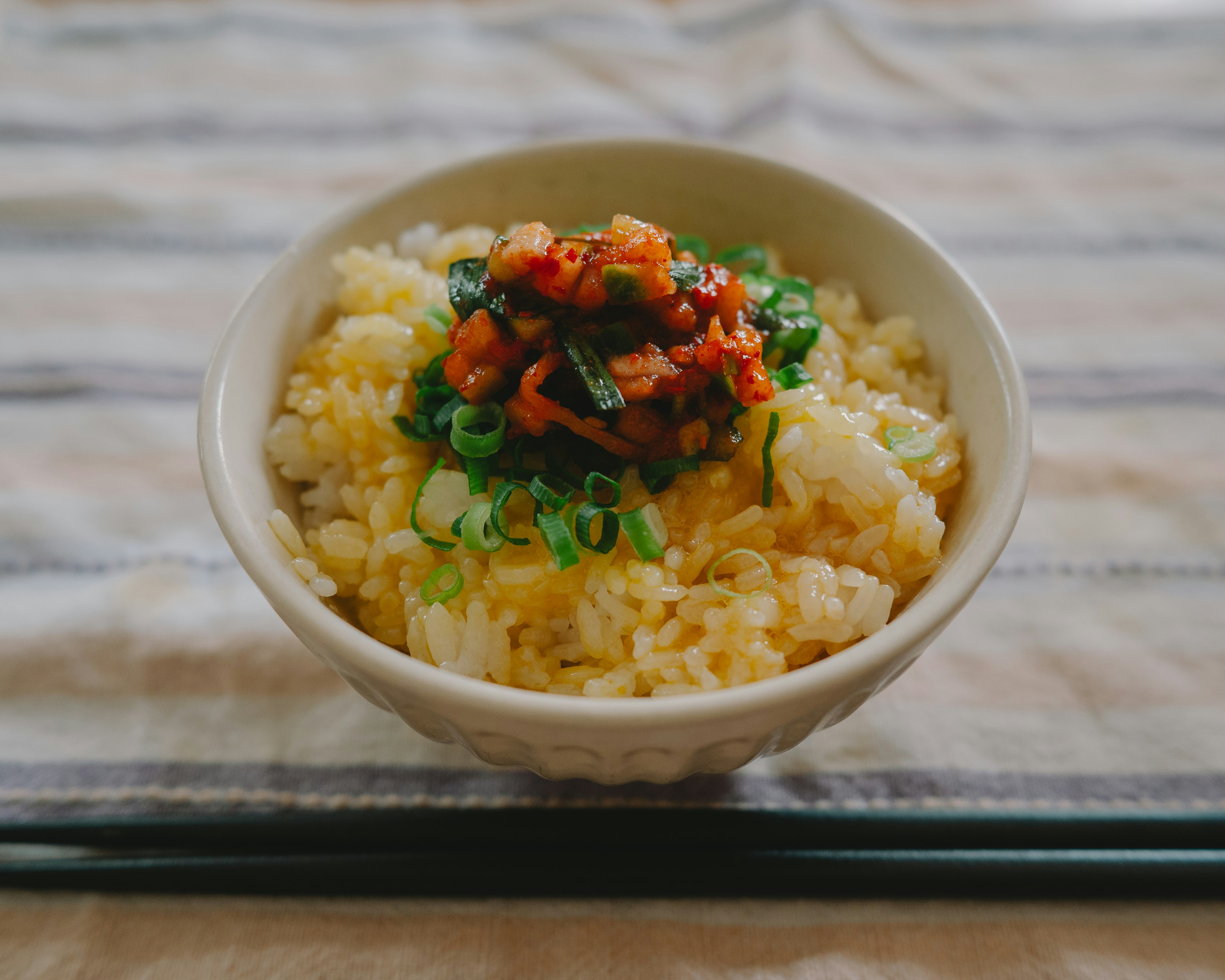 Bowl of rice topped with green onions and spicy meat