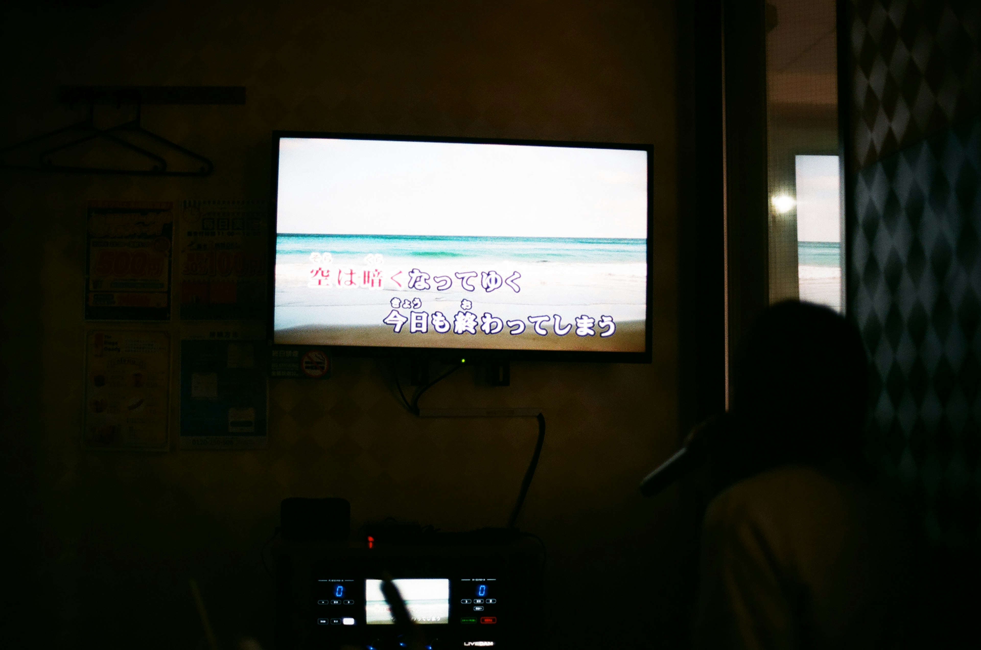 Layar televisi menampilkan pemandangan pantai dengan lirik karaoke