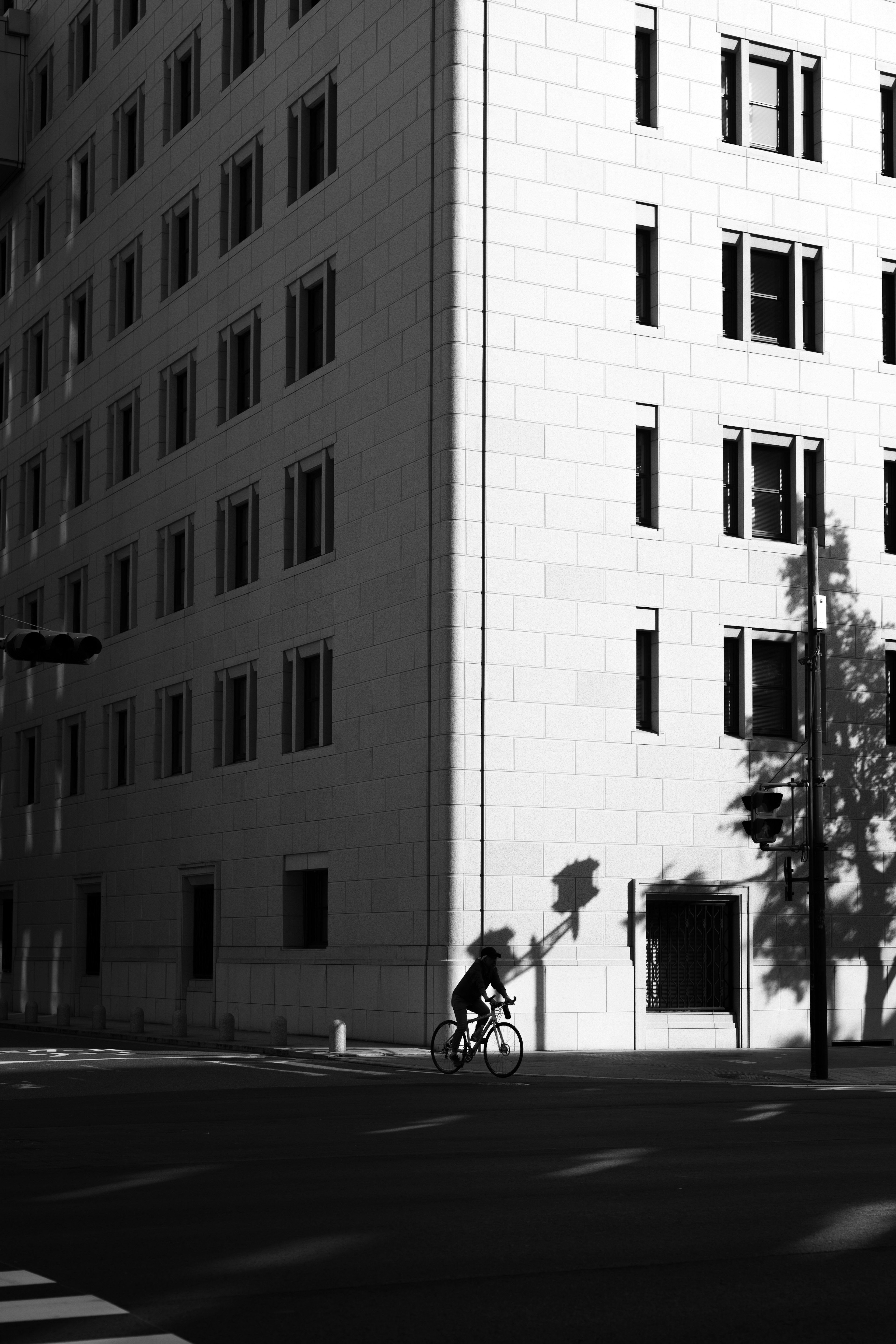 A person riding a bicycle at a street corner with a tall building shadow