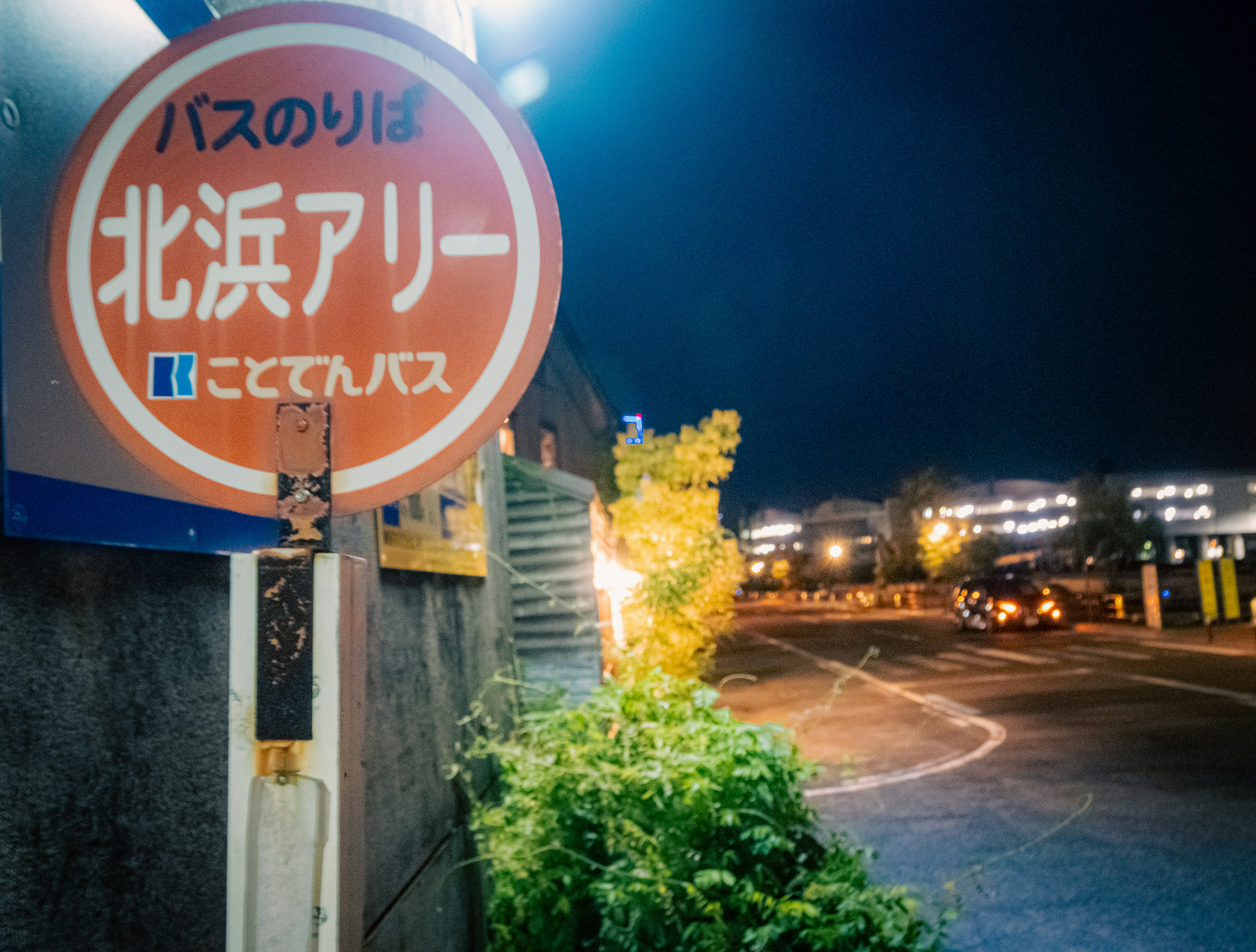 Señal de parada de autobús para Kitahama Alley de noche rodeada de vegetación y farolas