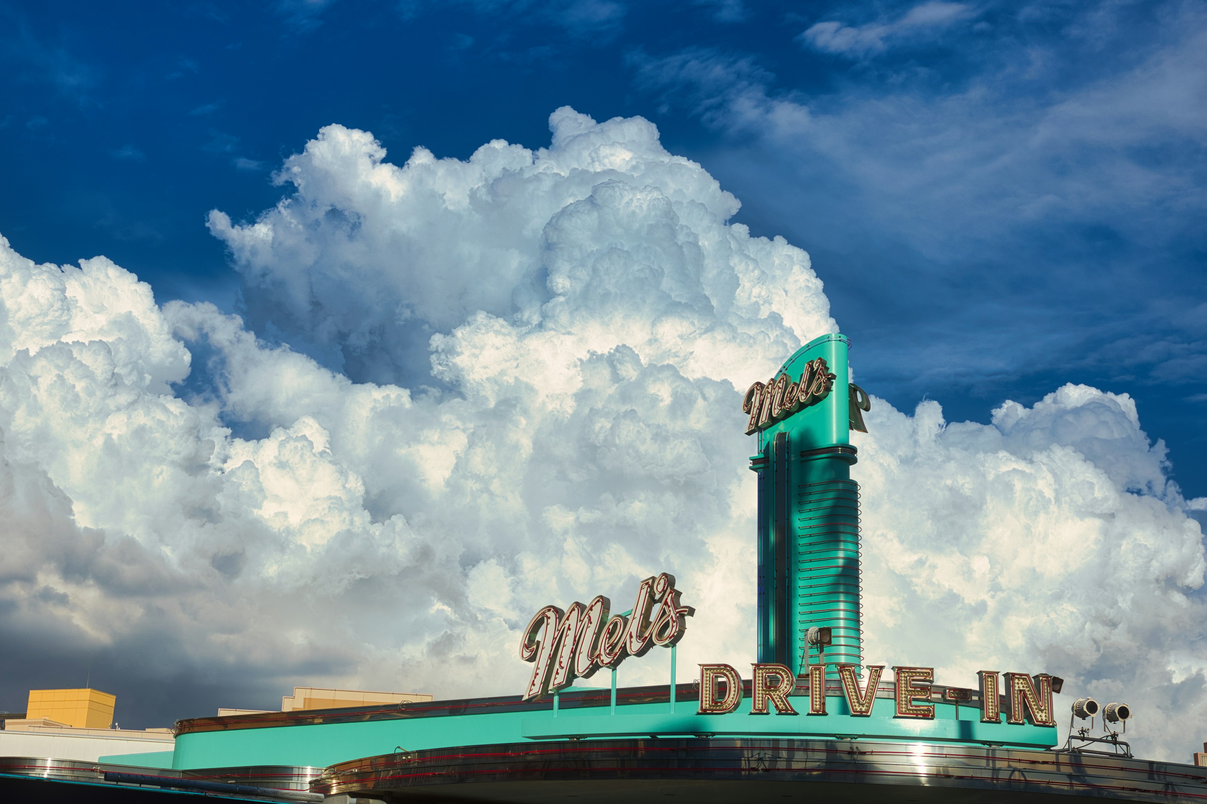 Retro sign of Mel's Drive-In under a blue sky with clouds