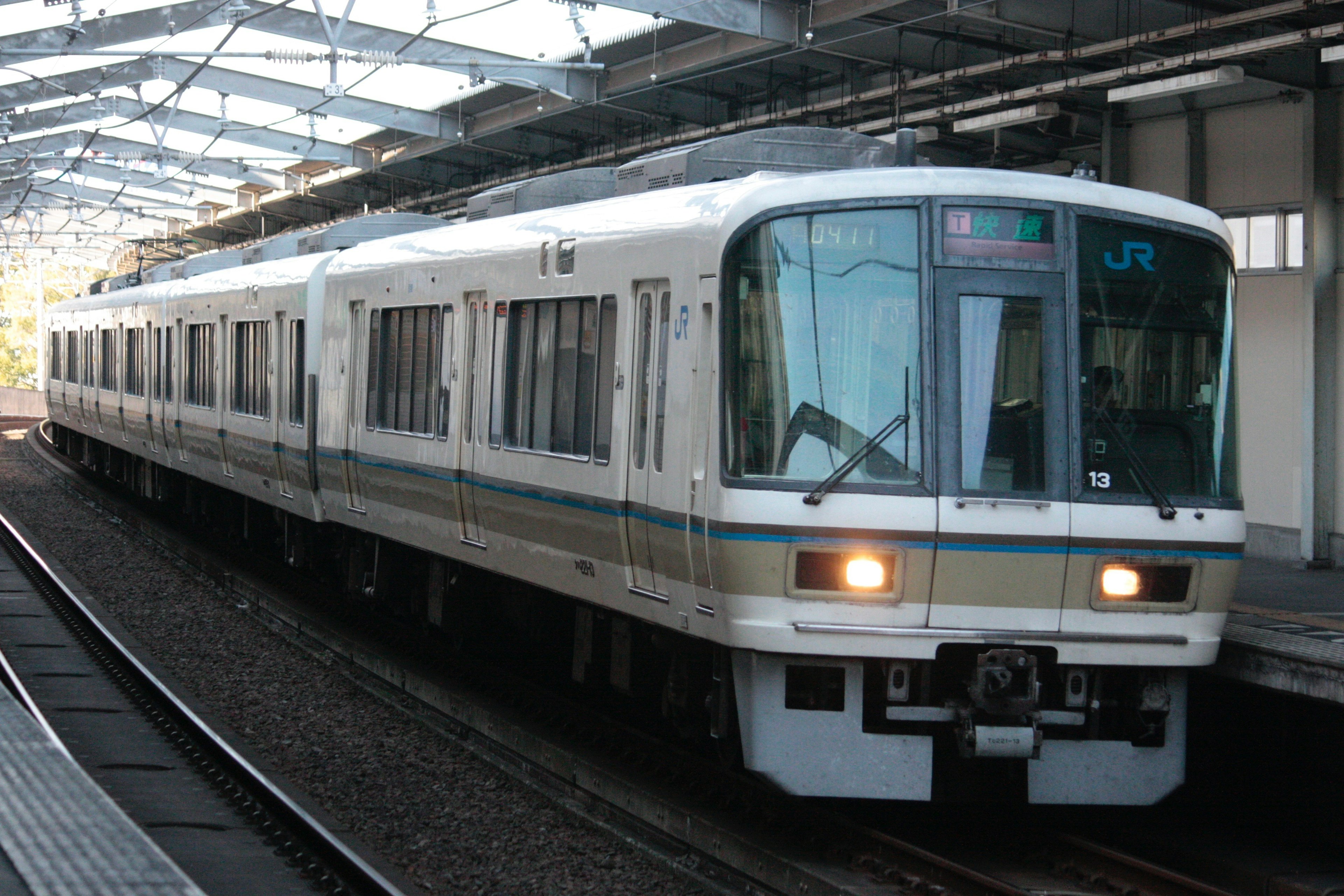 A white train is stopped at a station with a metal roof structure overhead