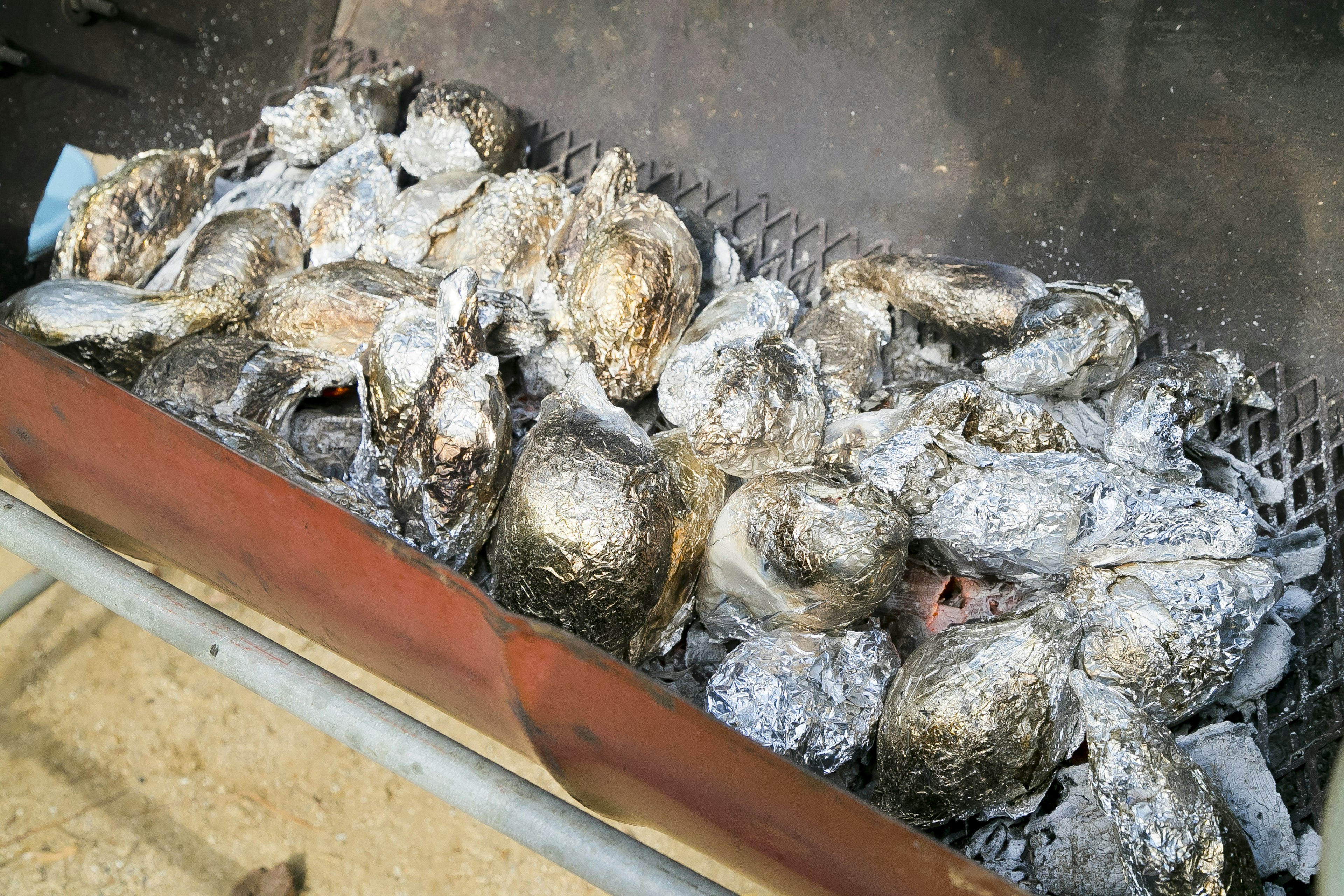 Fischköpfe, die in silberner Folie gewickelt auf einem Grill garen