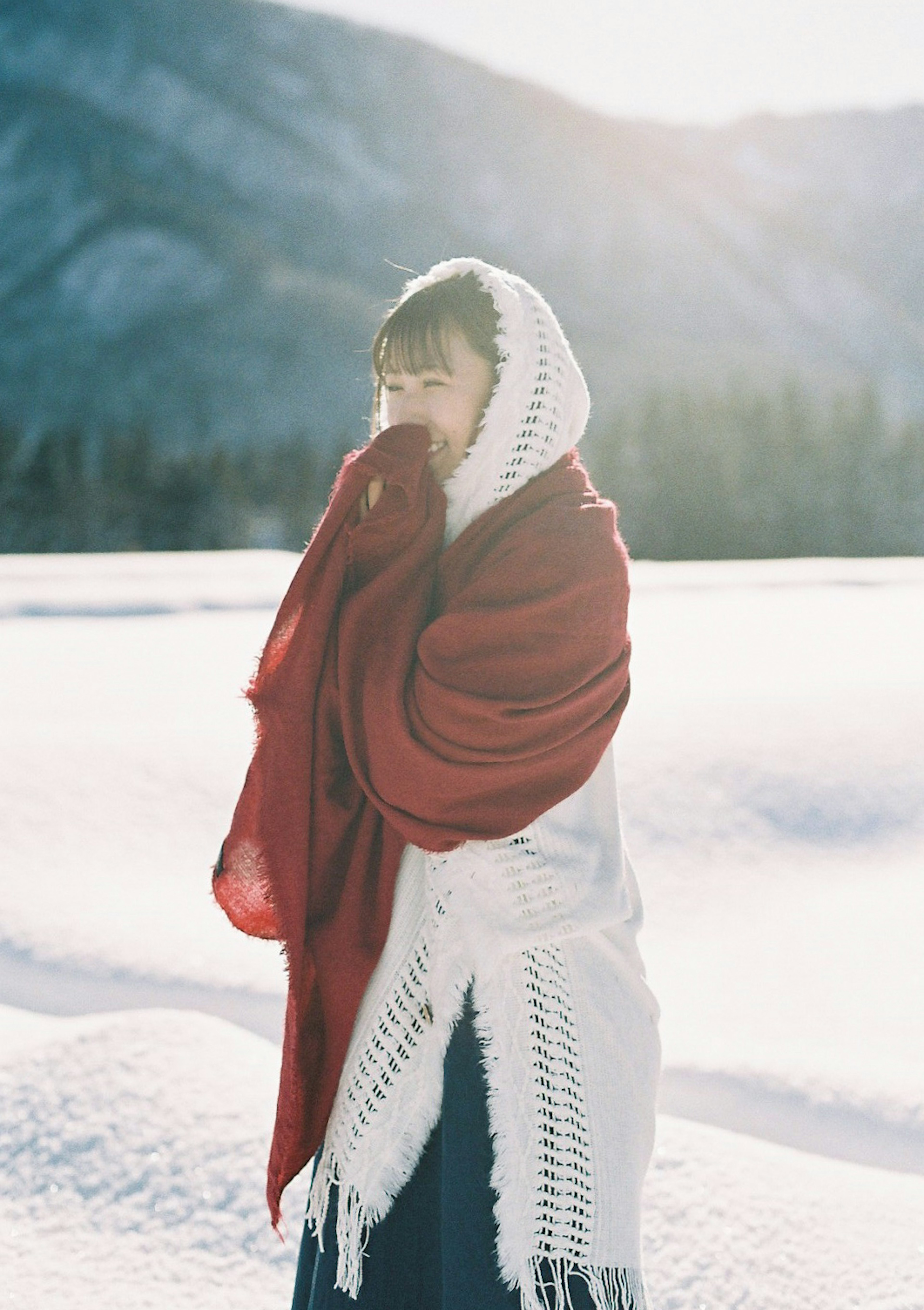 Woman wrapped in a red shawl standing in snow with mountains in the background