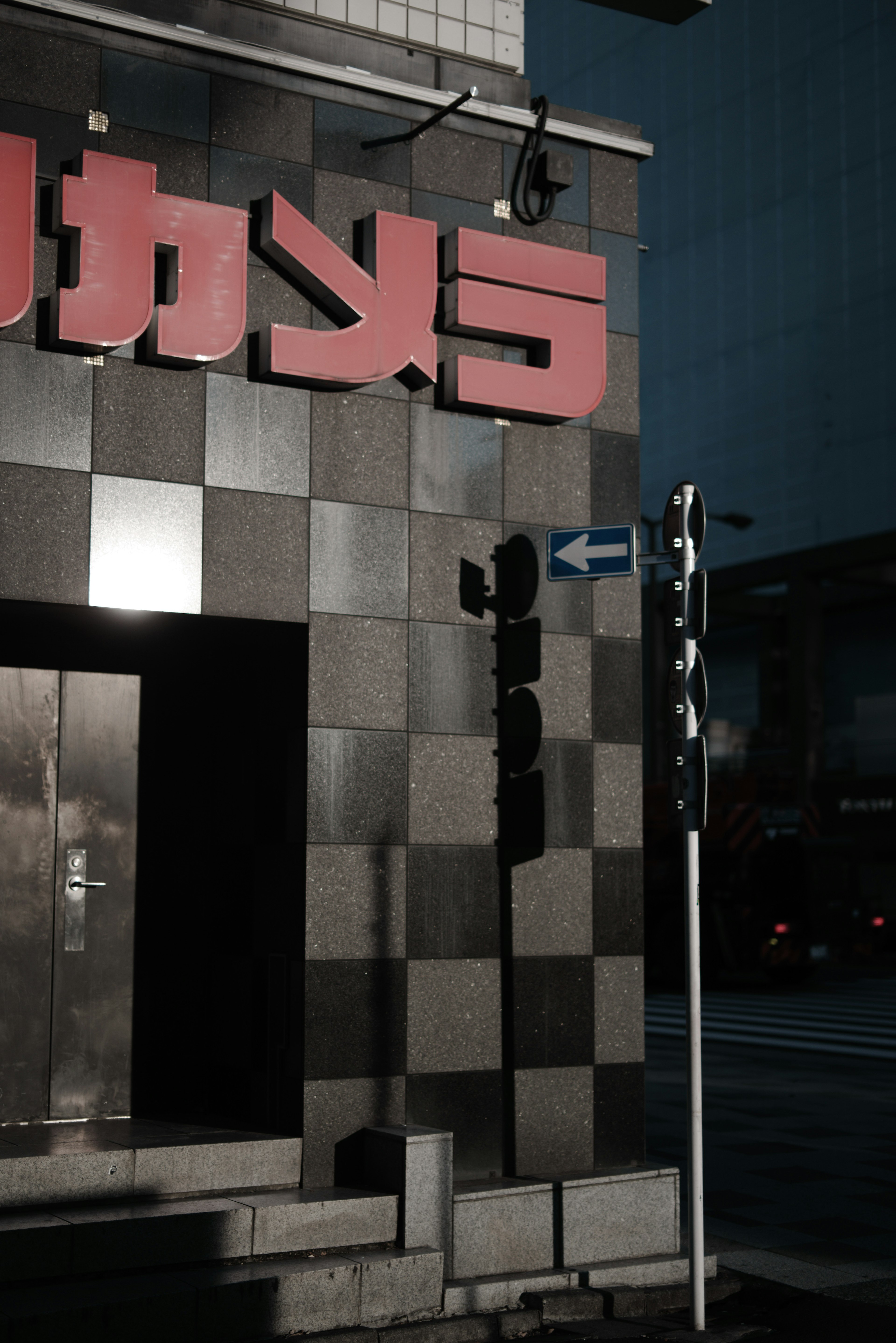 Street corner view featuring a building with a red sign and a traffic light in low light