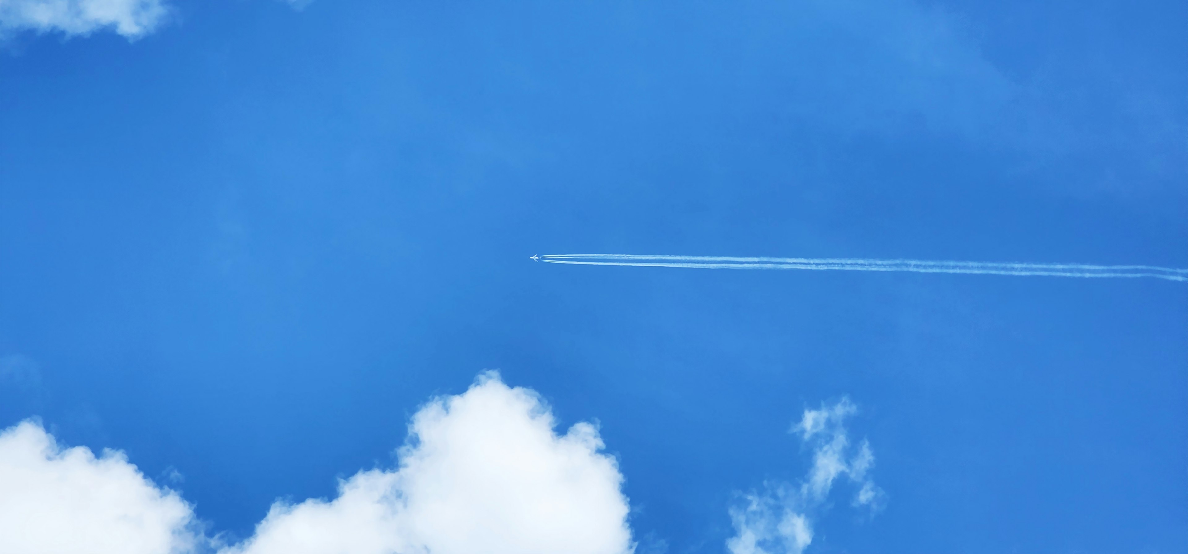 Langit biru cerah dengan jejak pesawat dan awan putih berbulu