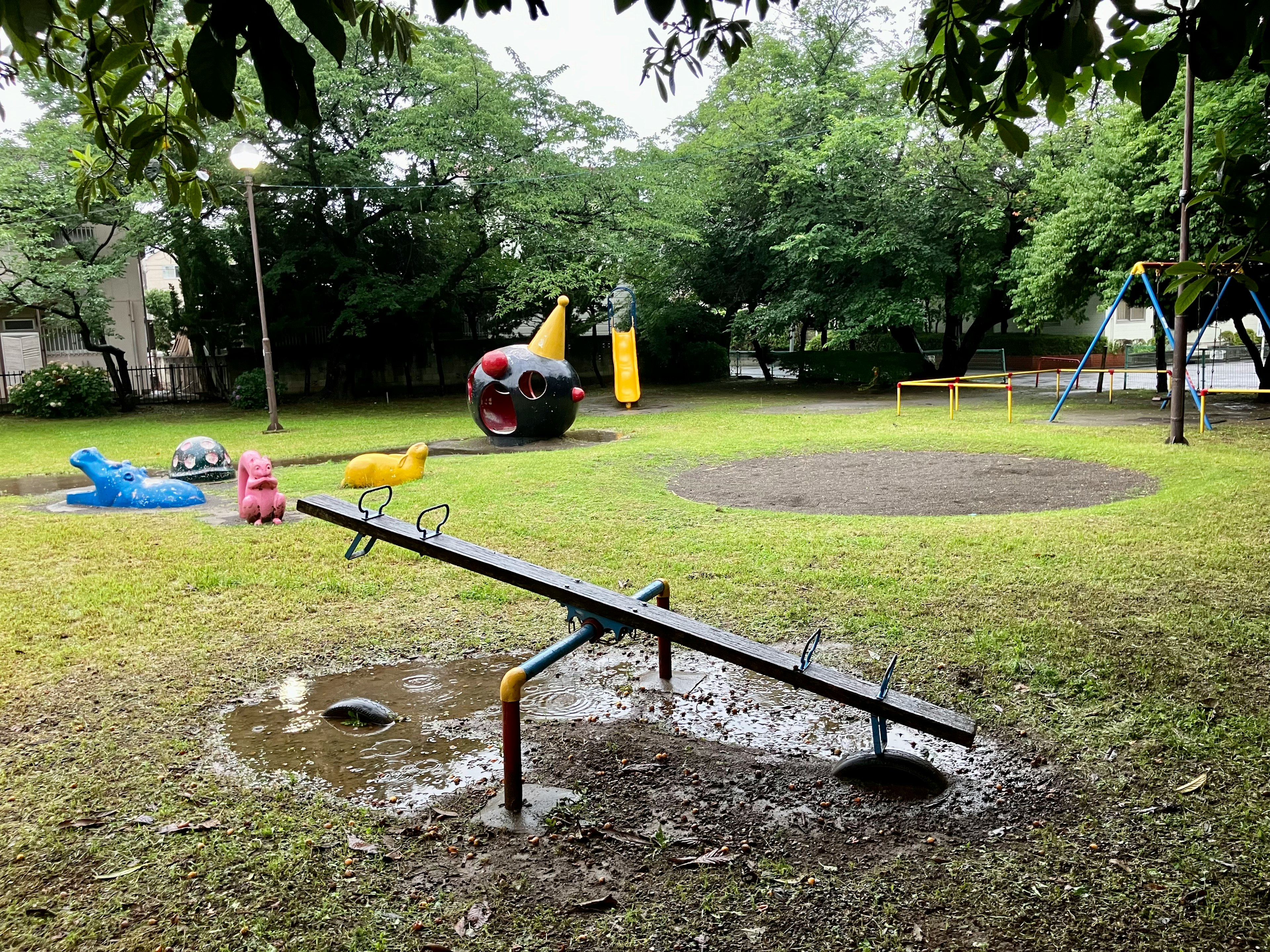 遊び場の滑り台とシーソーのある緑豊かな公園の風景