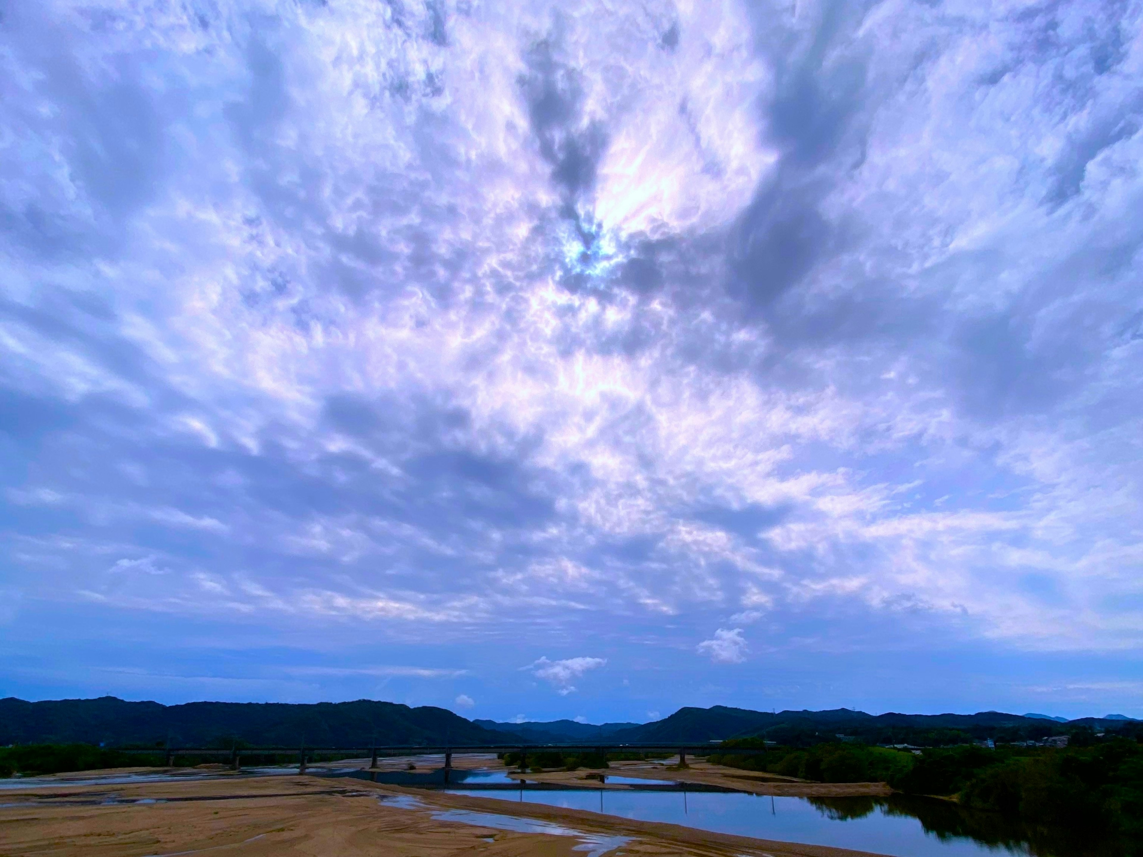 Pemandangan langit biru dengan awan sungai mengalir dikelilingi perbukitan hijau