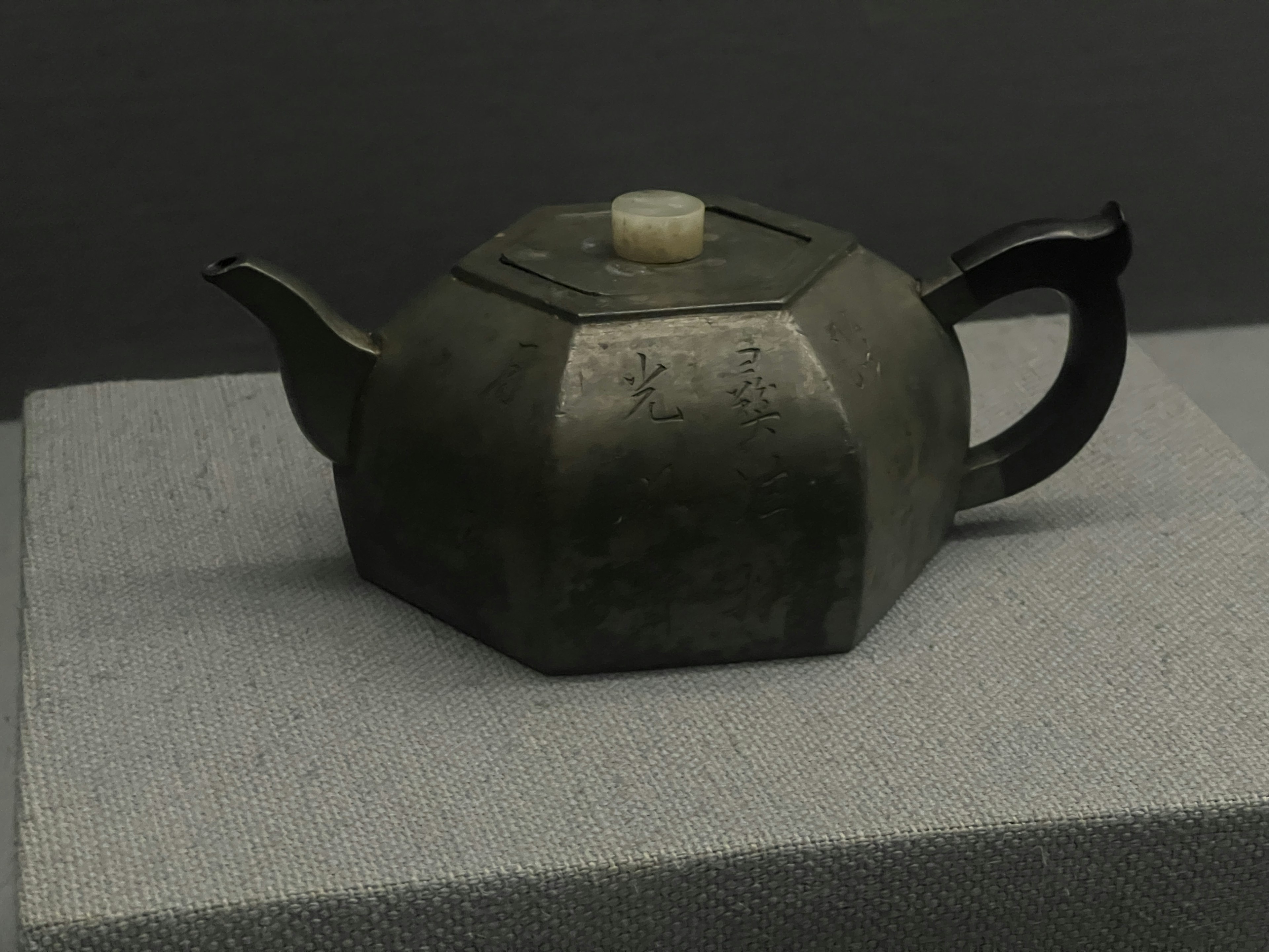 Hexagonal metal teapot placed on a gray fabric surface