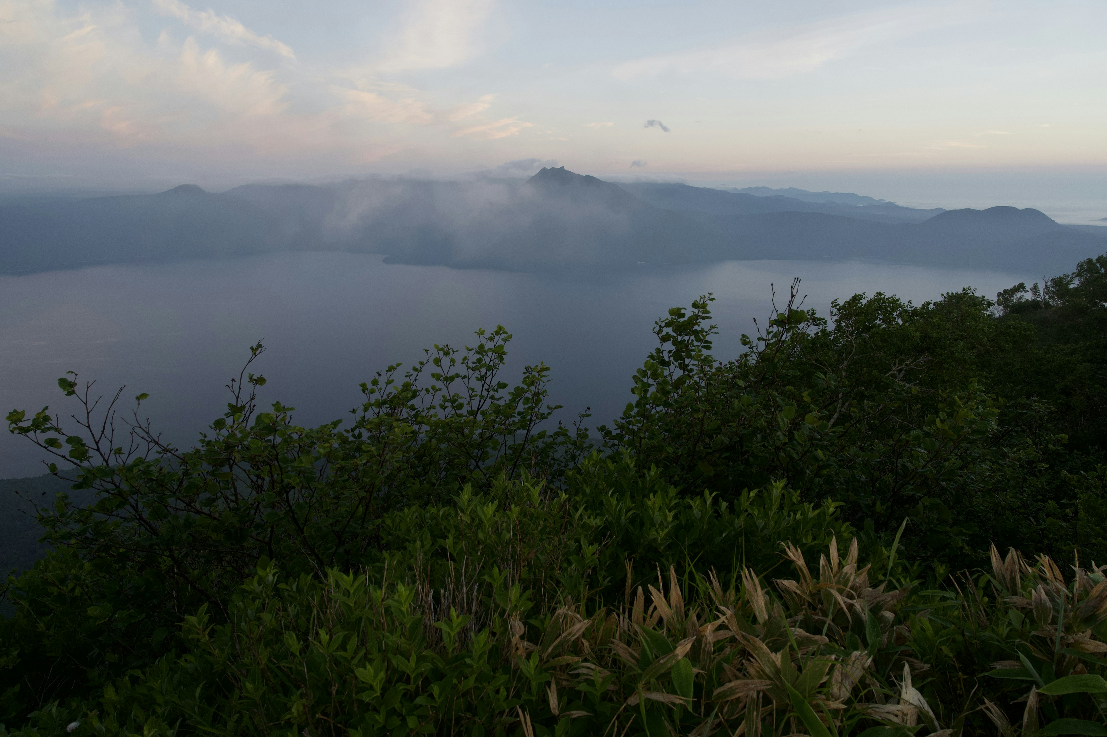 Malersicher Blick auf einen See umgeben von Bergen und Nebel