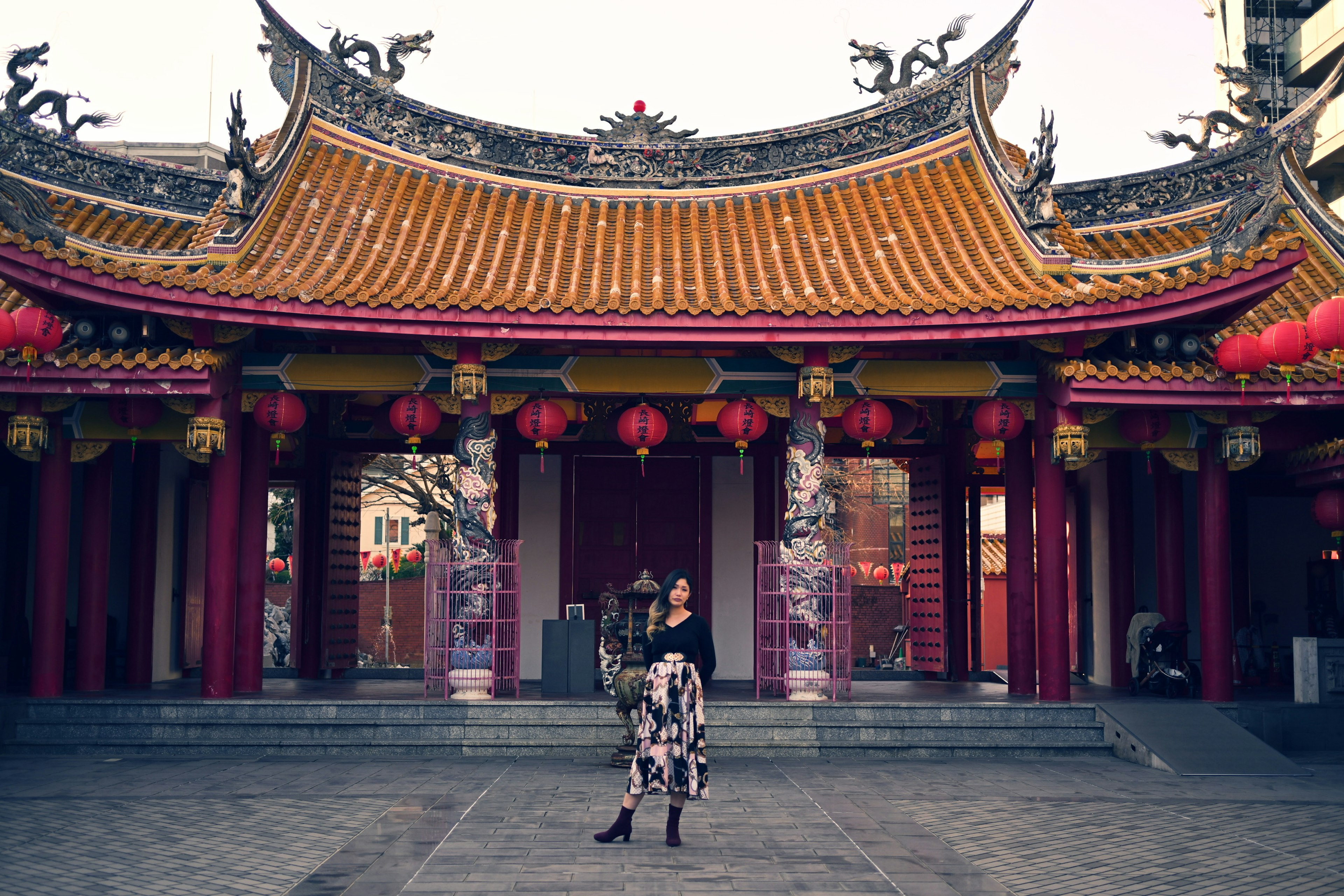 Mujer de pie frente a un templo chino tradicional con faroles rojos vibrantes