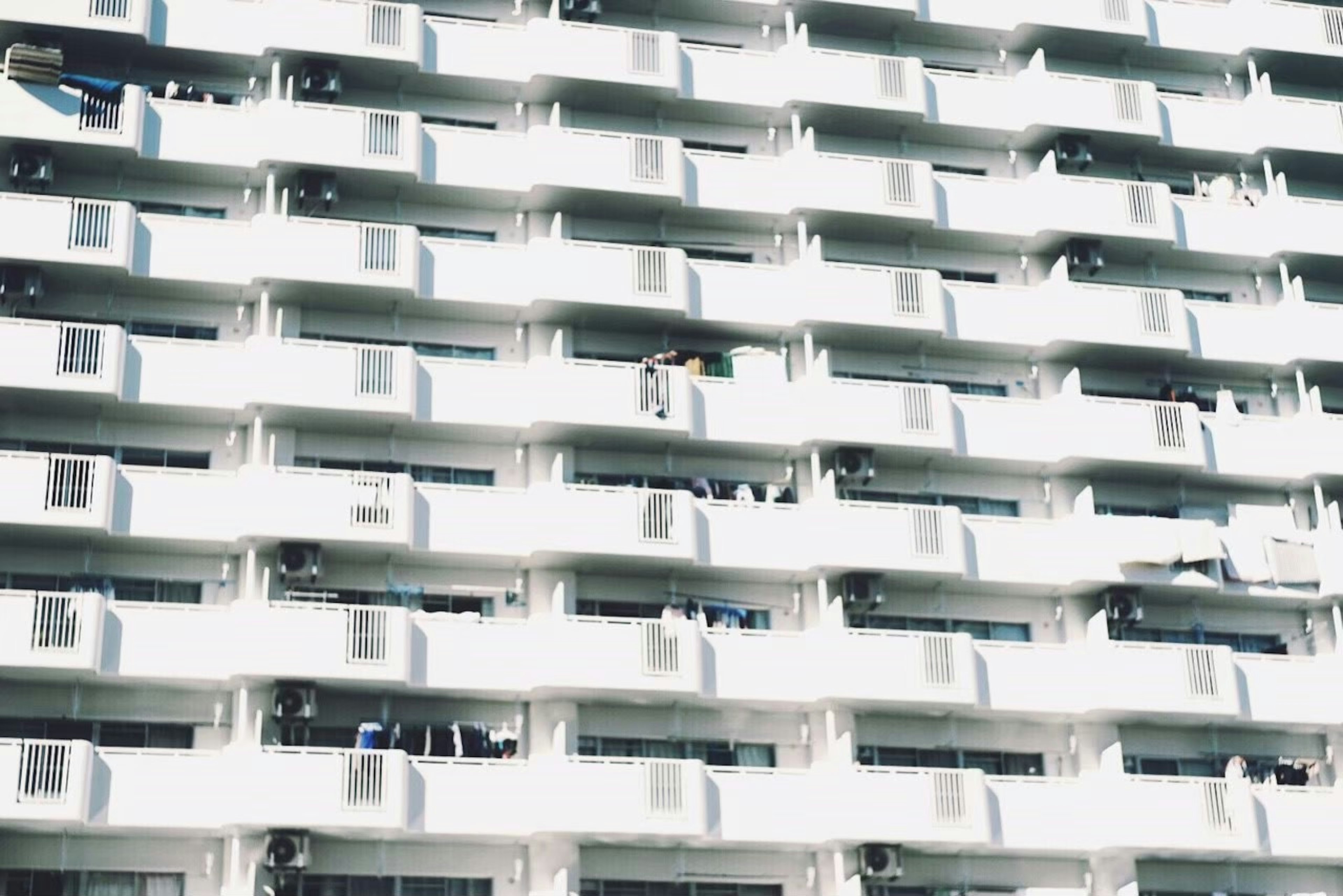 Fachada blanca de un edificio con filas de balcones y unidades de aire acondicionado