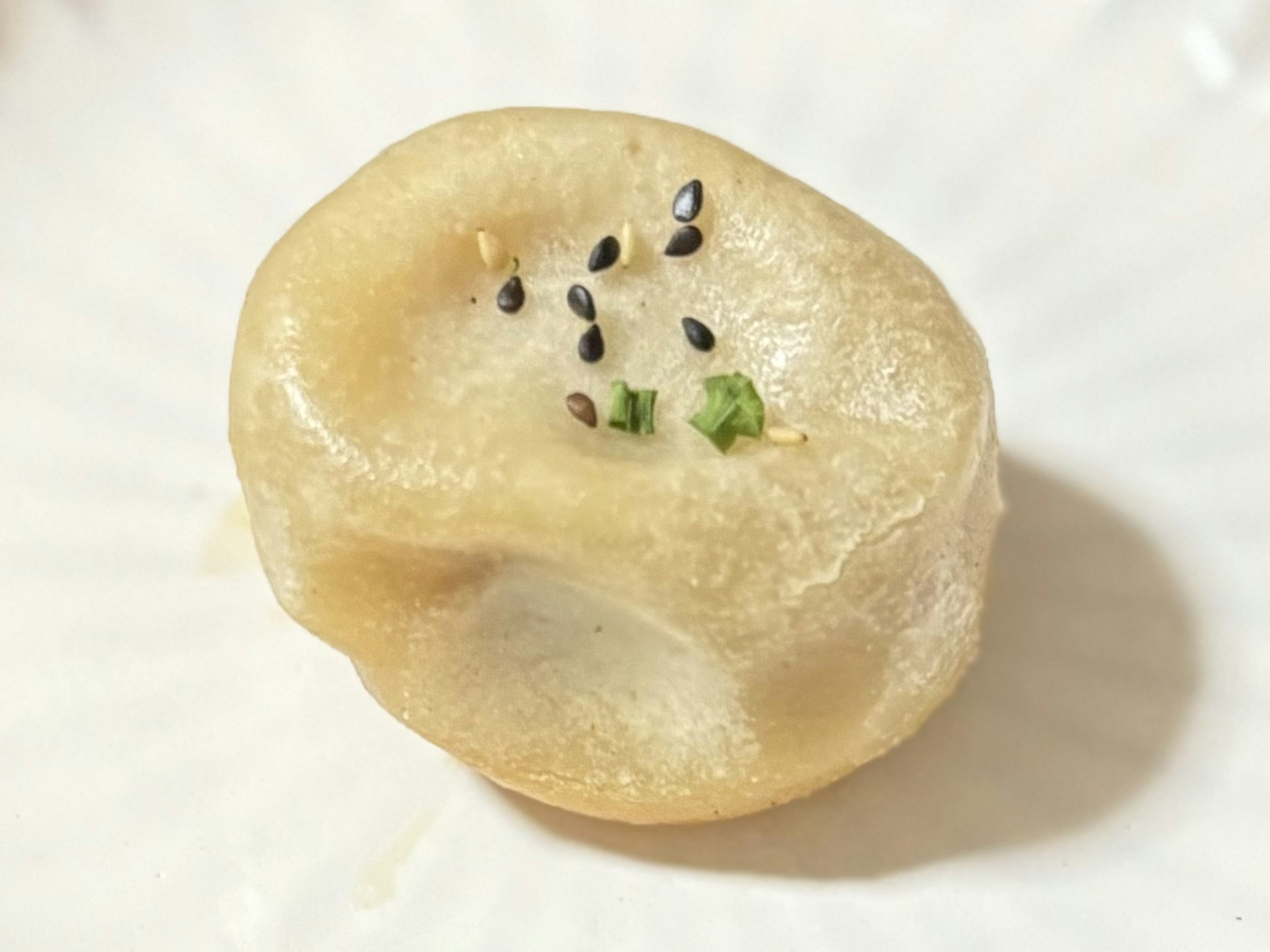 Runde dumplingartige Speise auf einem weißen Teller mit schwarzem Sesam und grünen Zwiebeln garniert