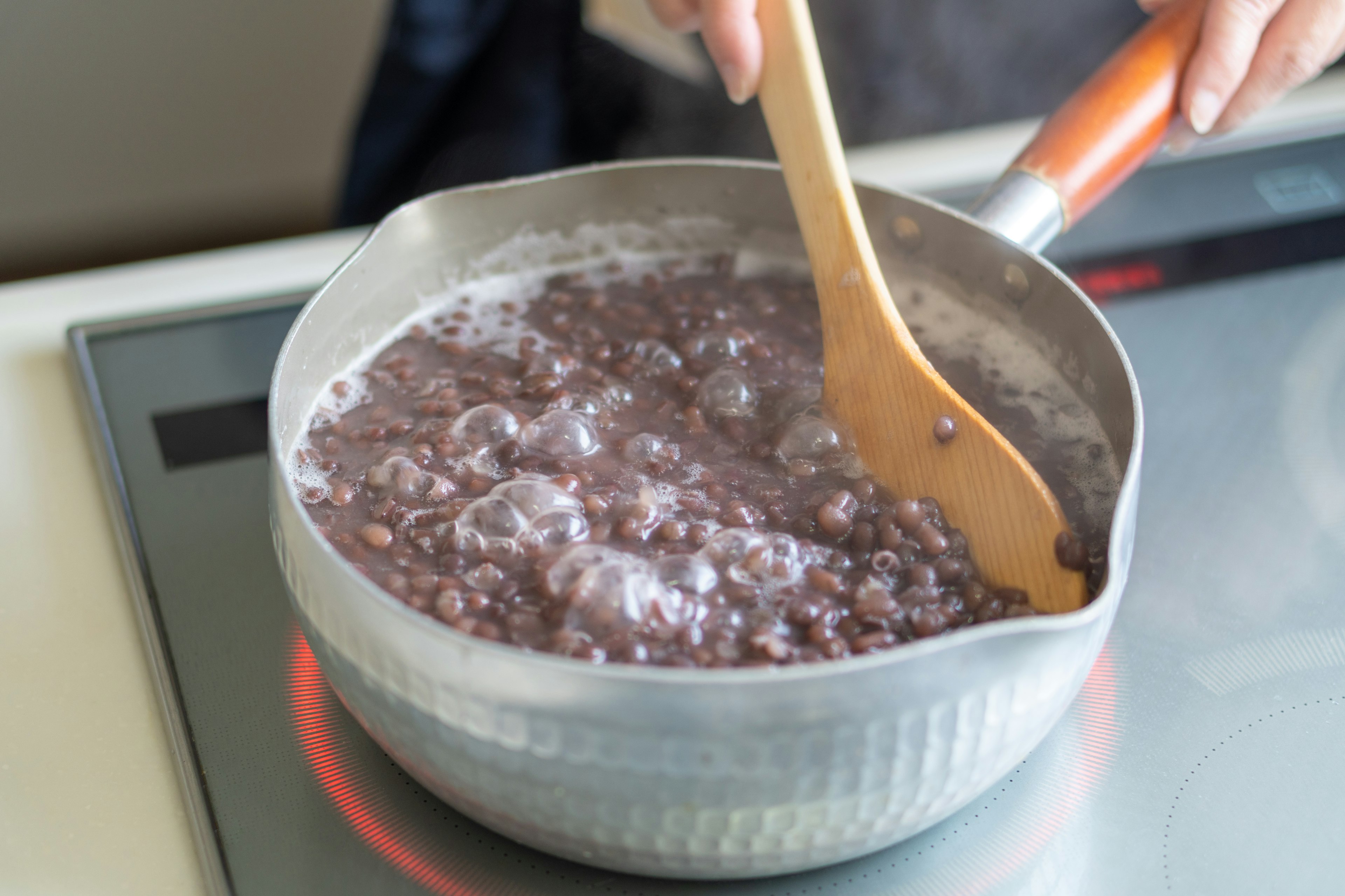 Main remuant une soupe de haricots rouges dans une casserole sur une cuisinière