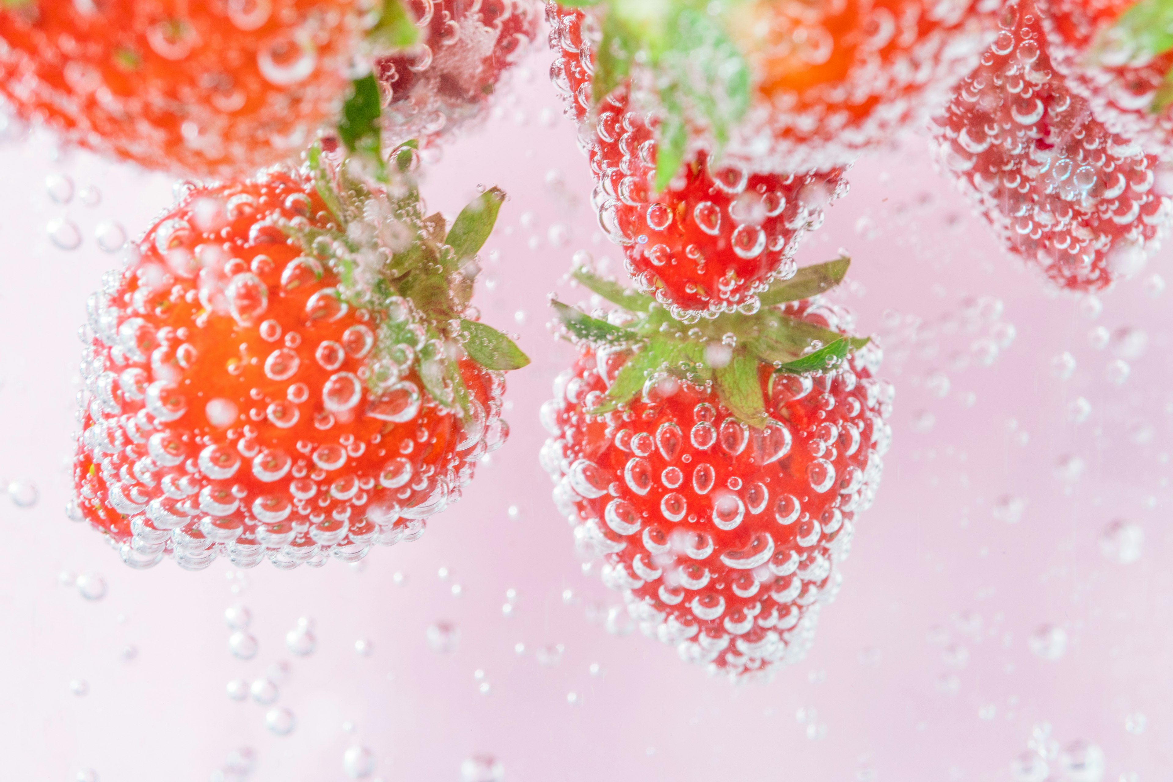 Fresh strawberries floating in bubbles against a pink background