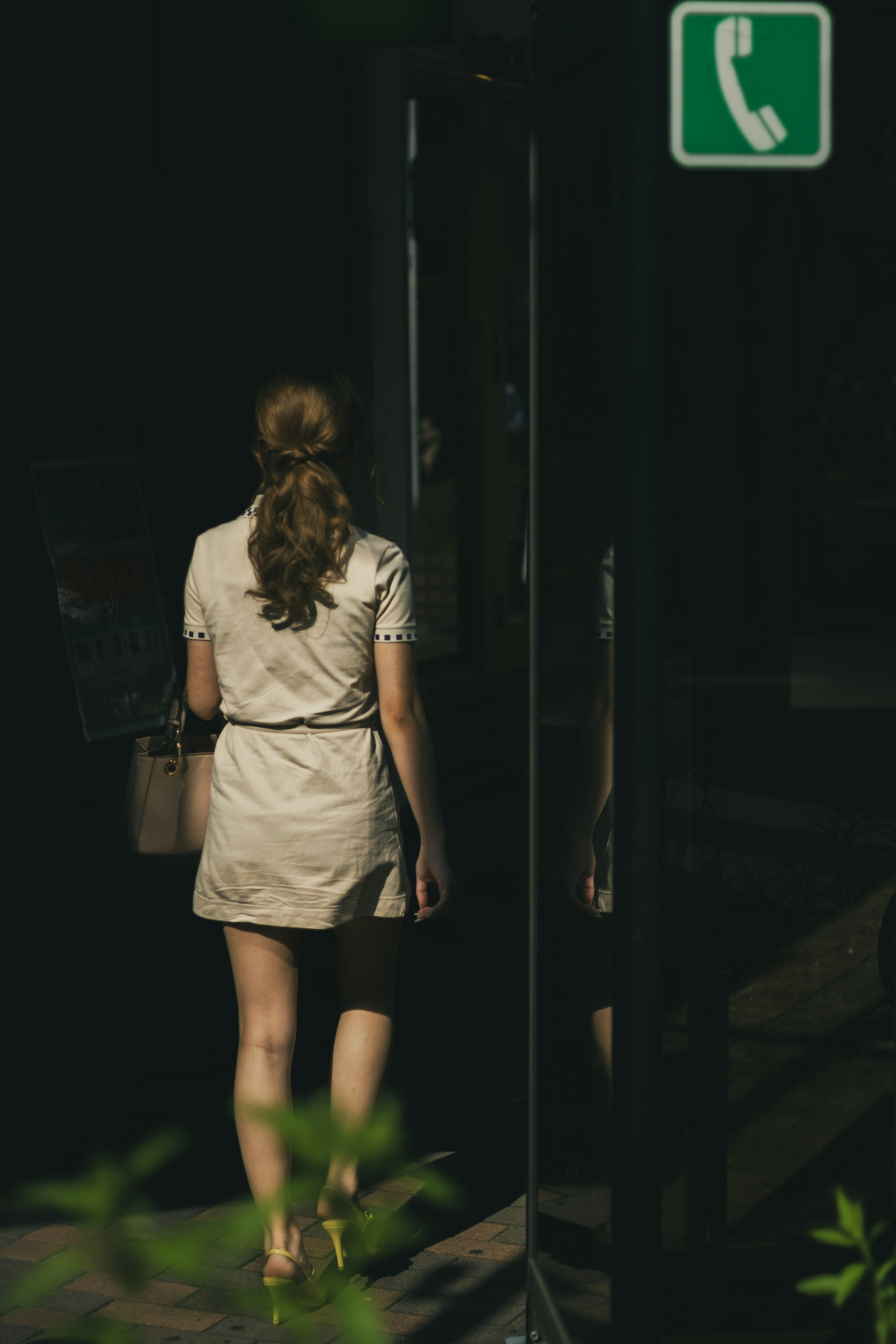 Una mujer caminando con un letrero de cabina telefónica visible