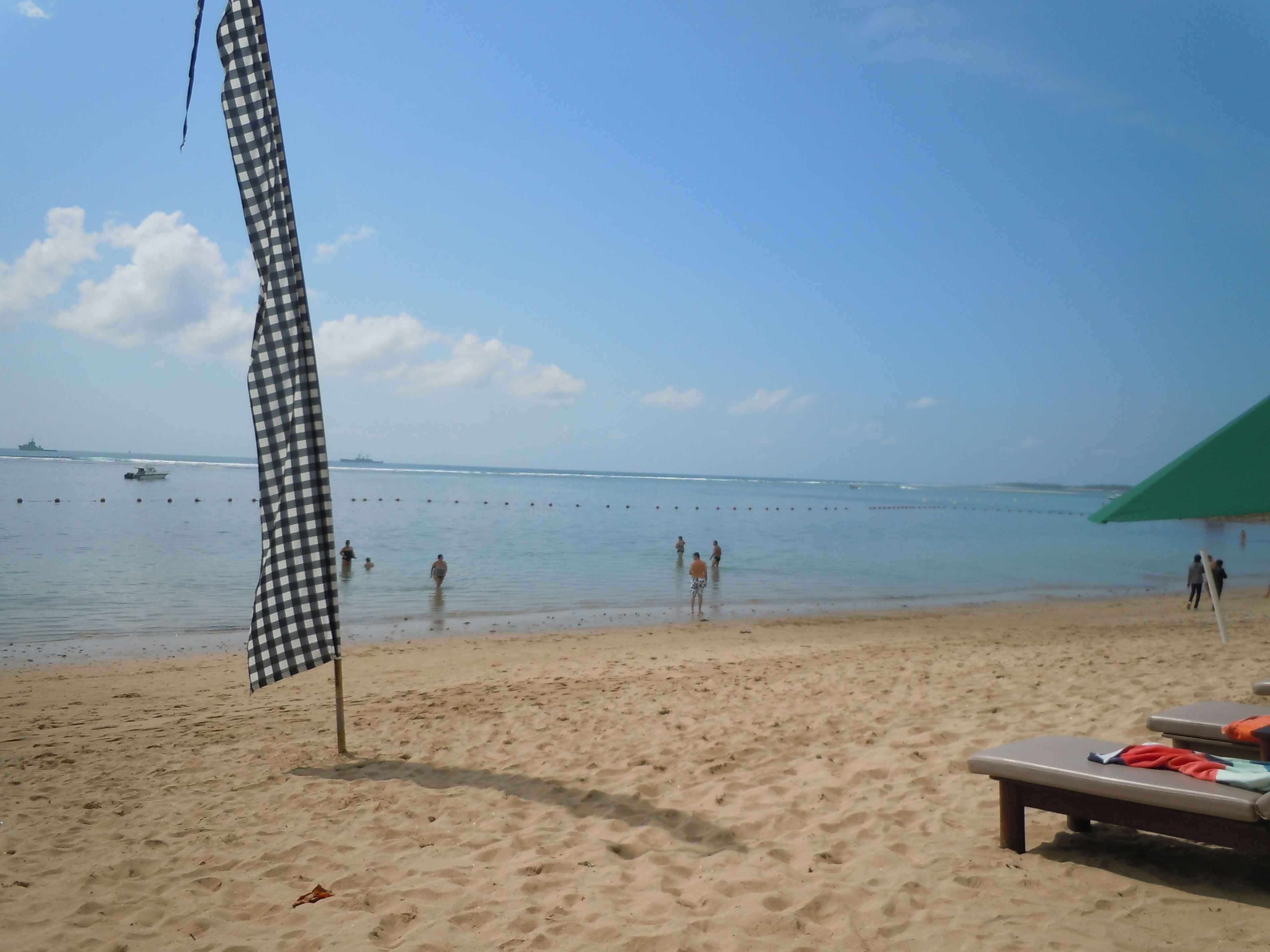 ฉากชายหาดท้องฟ้าสีฟ้าและทะเลชายหาดทรายมีเตียงอาบแดดและธงตาราง