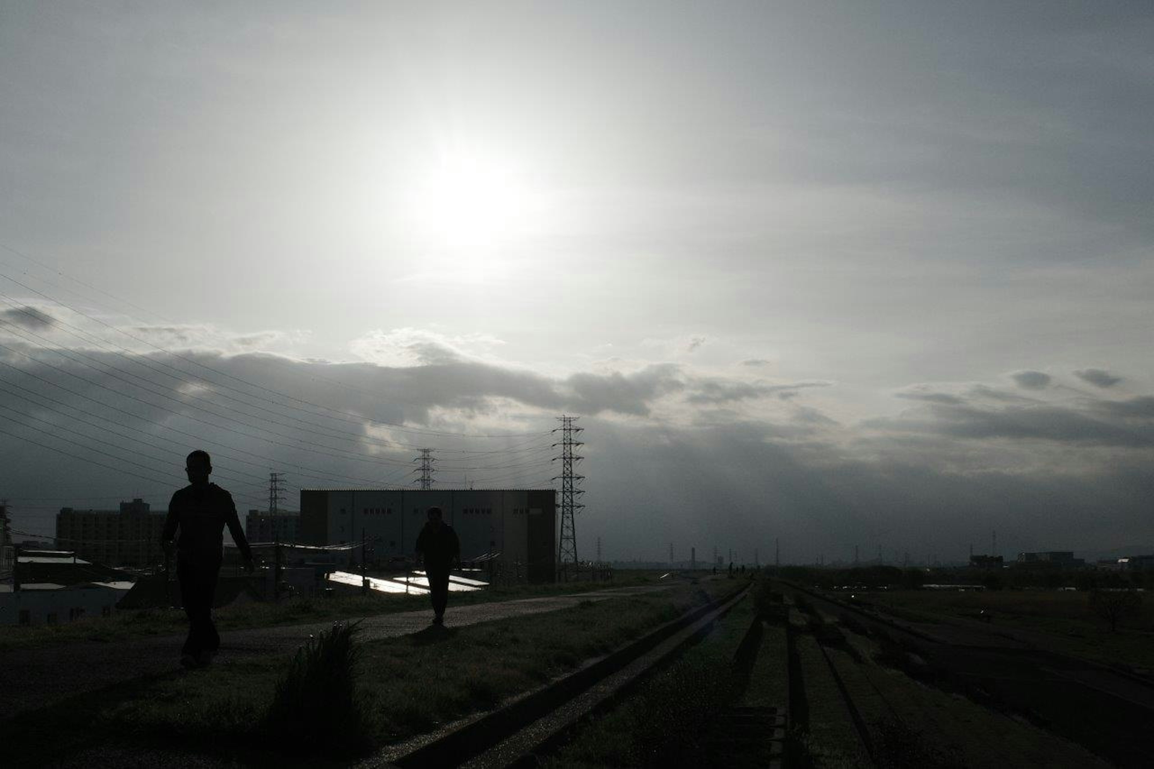 Silhouettes de personnes marchant le long d'une voie ferrée sous un ciel nuageux