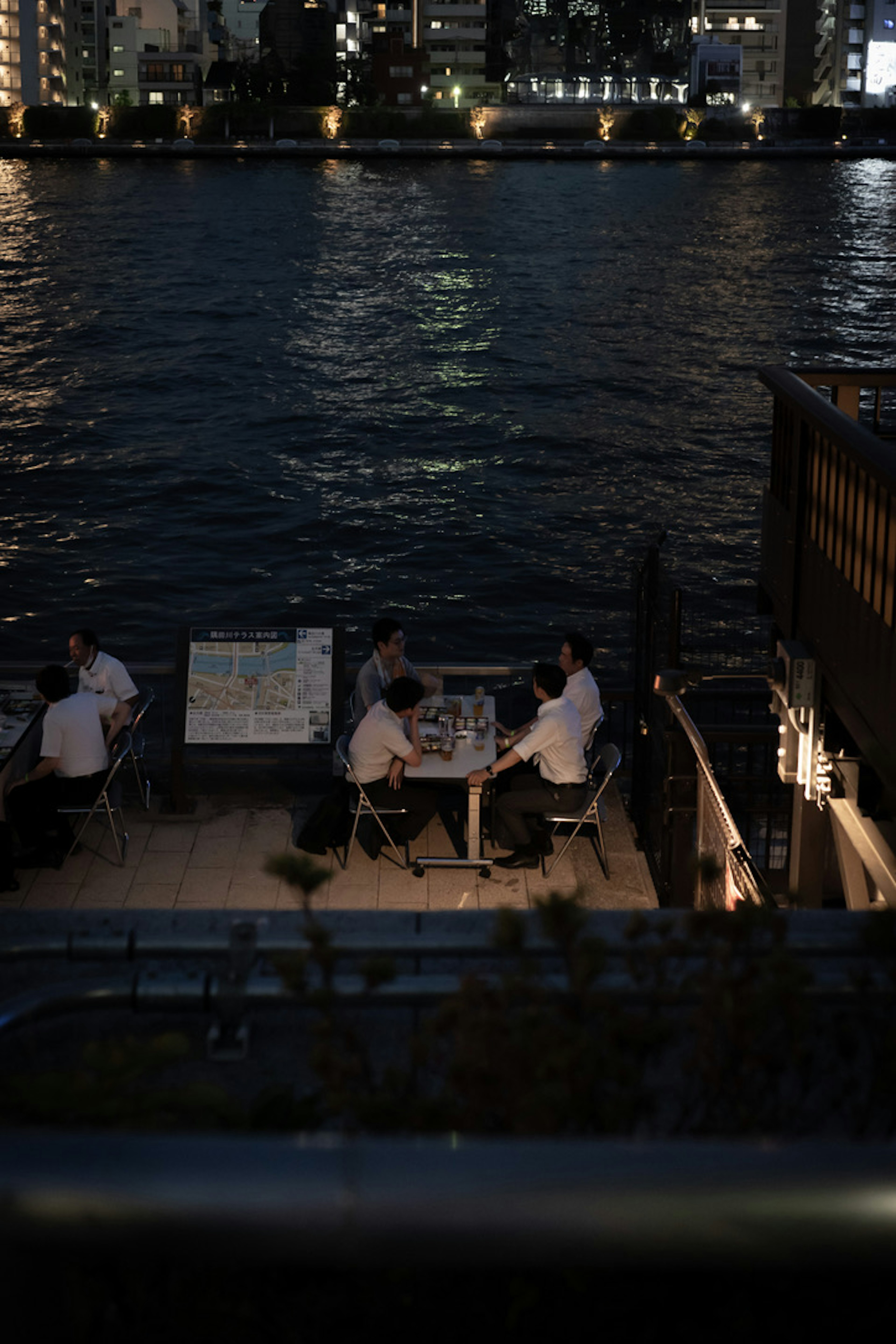 Personnes assises à une table au bord de l'eau la nuit avec des lumières de la ville